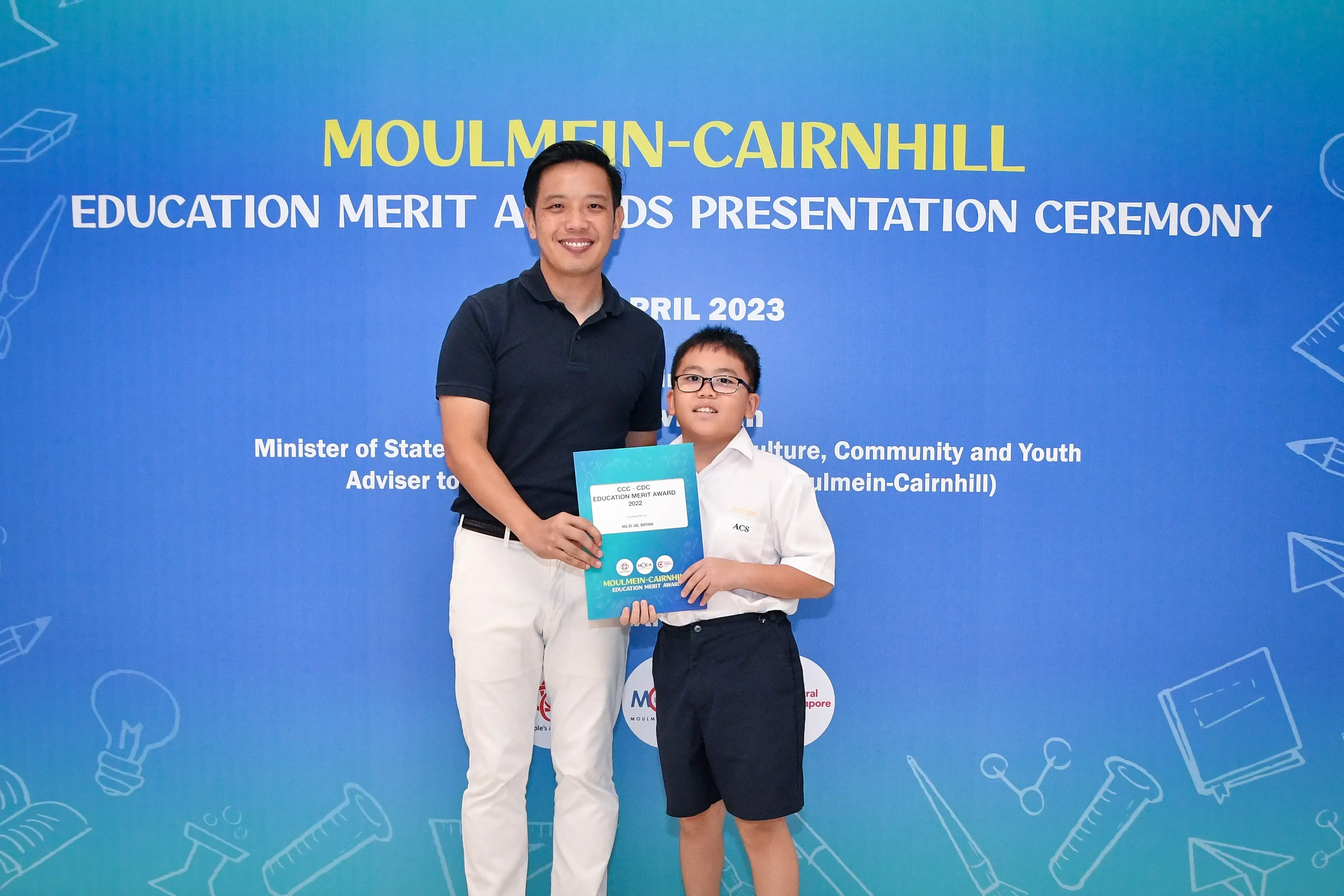 A man and a young boy holding an award certificate at the Moulmein-Cairnhill Education Merit Awards Ceremony 2023.