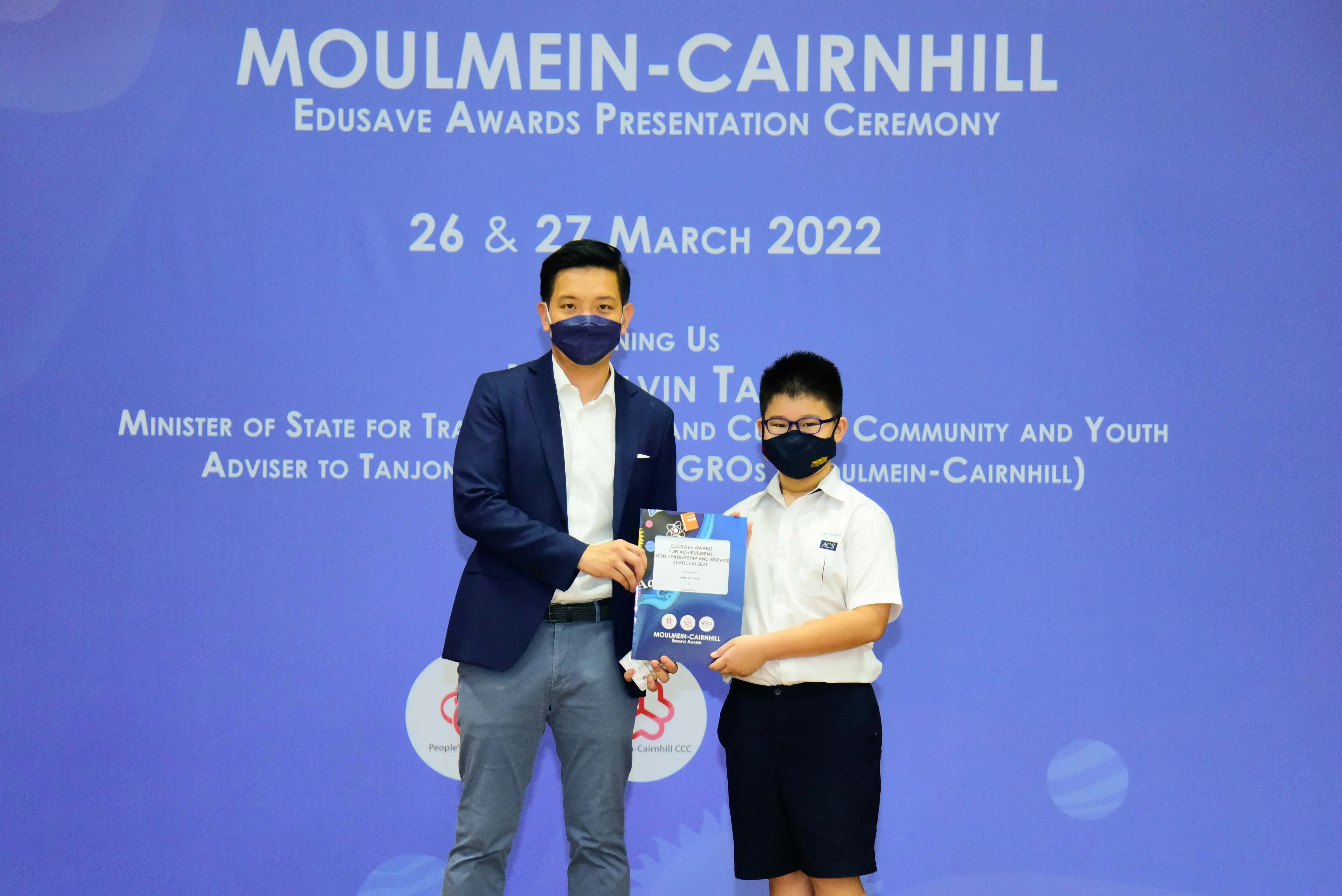 An adult and a student in masks hold an award booklet at the Moulmein-Cairnhill Edusave Awards Ceremony, March 2022.