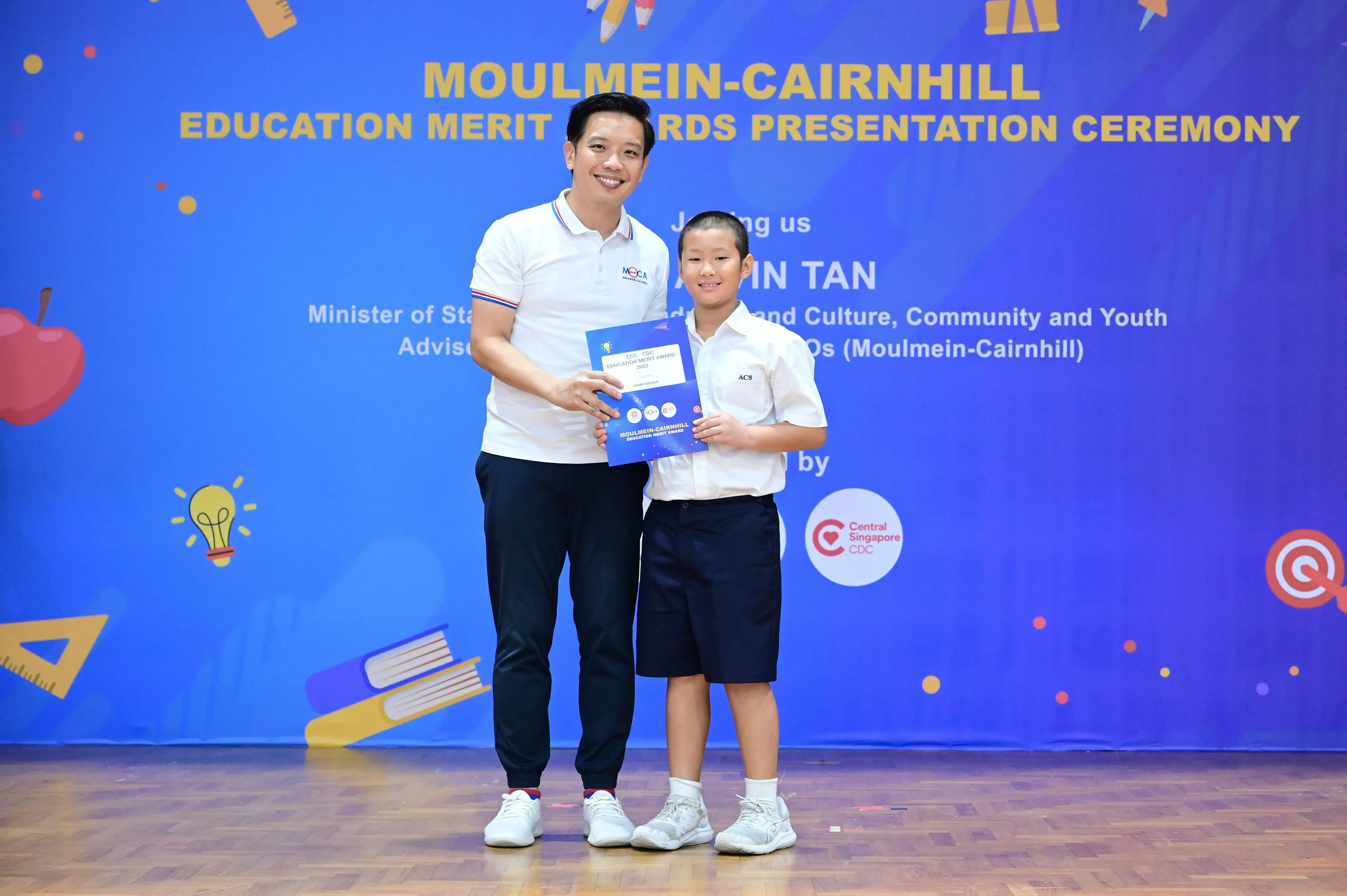 An adult and a young boy hold a certificate at the Moulmein-Cairnhill Education Merit Awards Presentation Ceremony.
