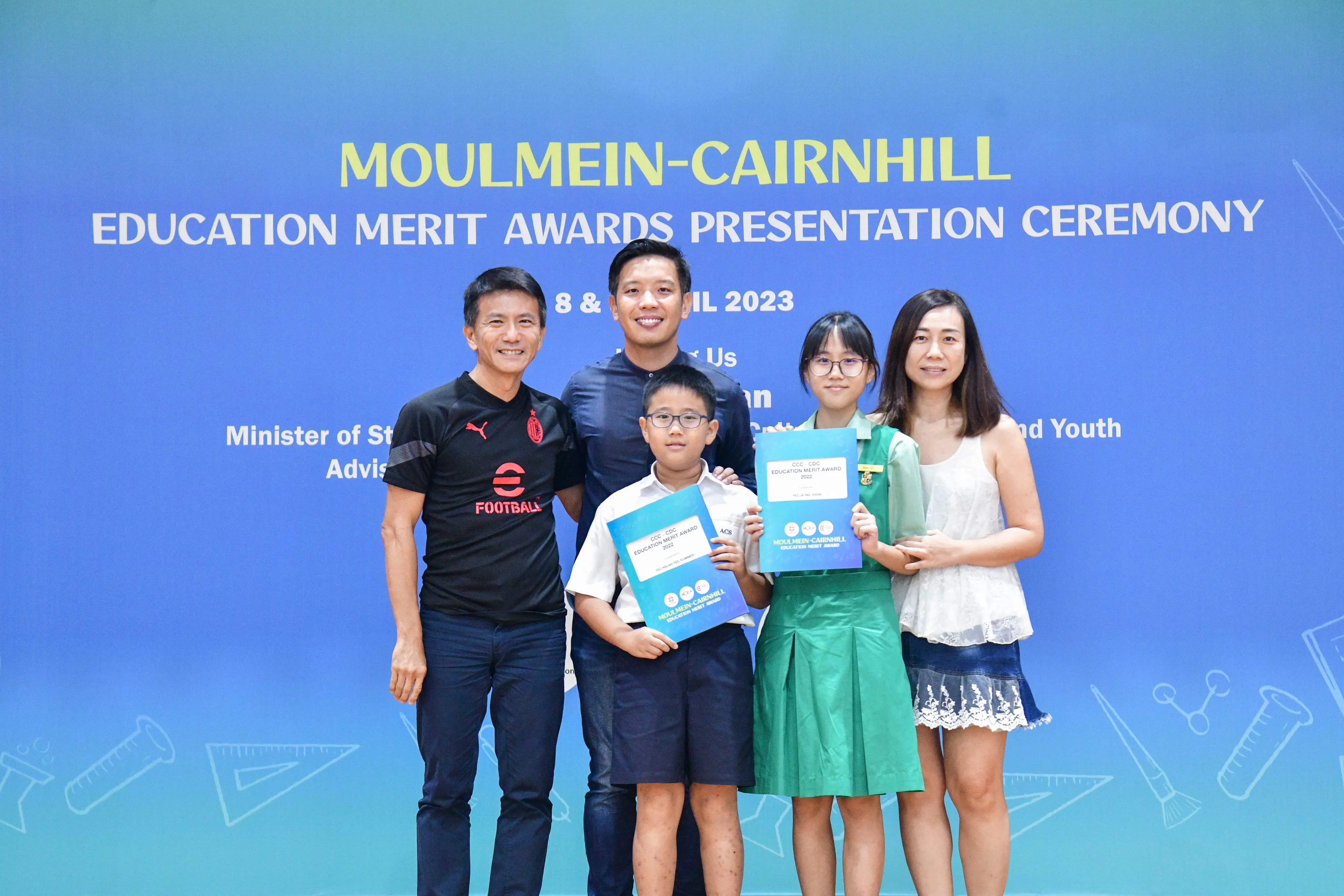 Five people pose at the Moulmein-Cairnhill Education Merit Awards Presentation Ceremony 2023, two children holding award certificates.