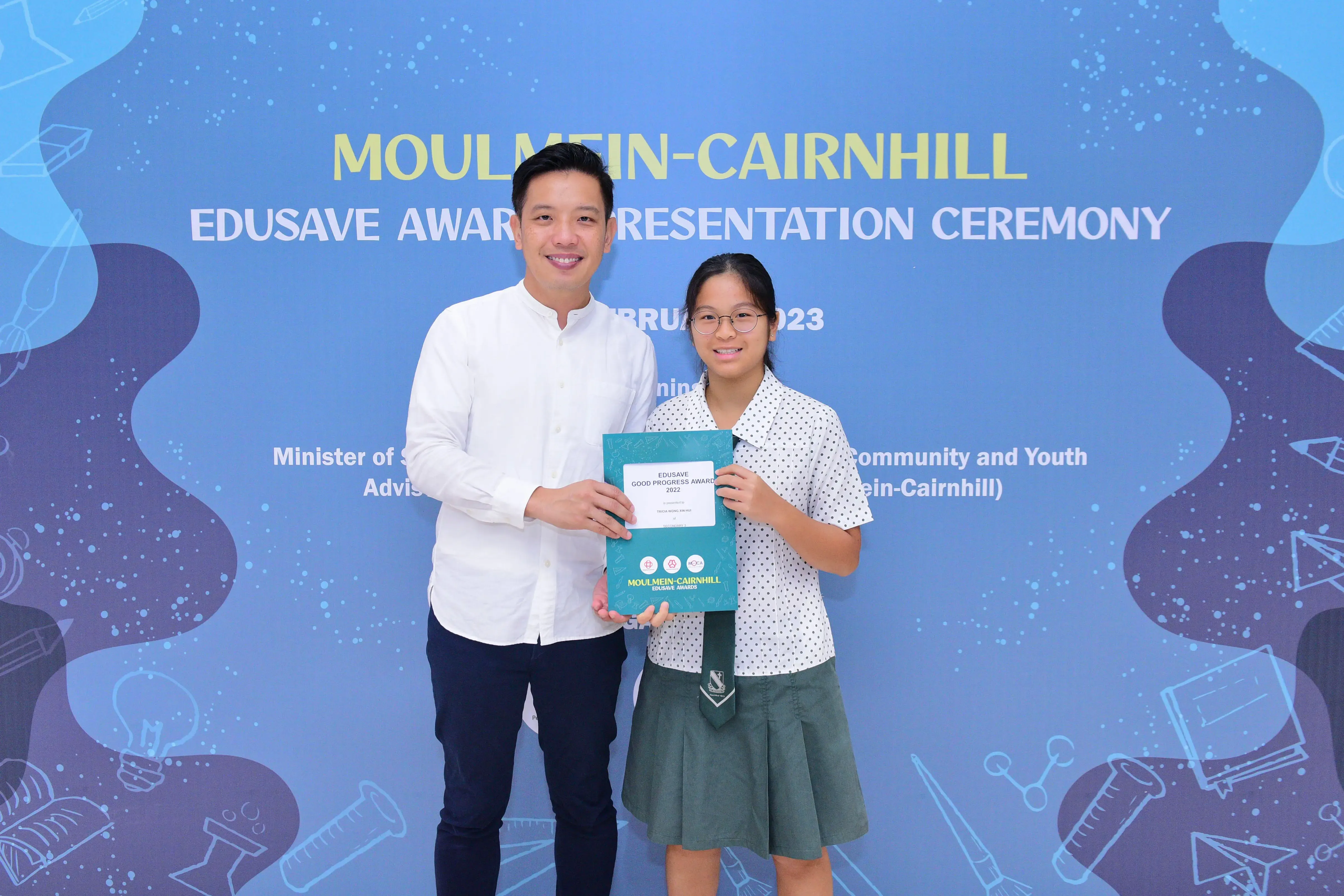 A man and a young girl hold an Edusave award certificate at the Moulmein-Cairnhill Award Presentation Ceremony 2023.