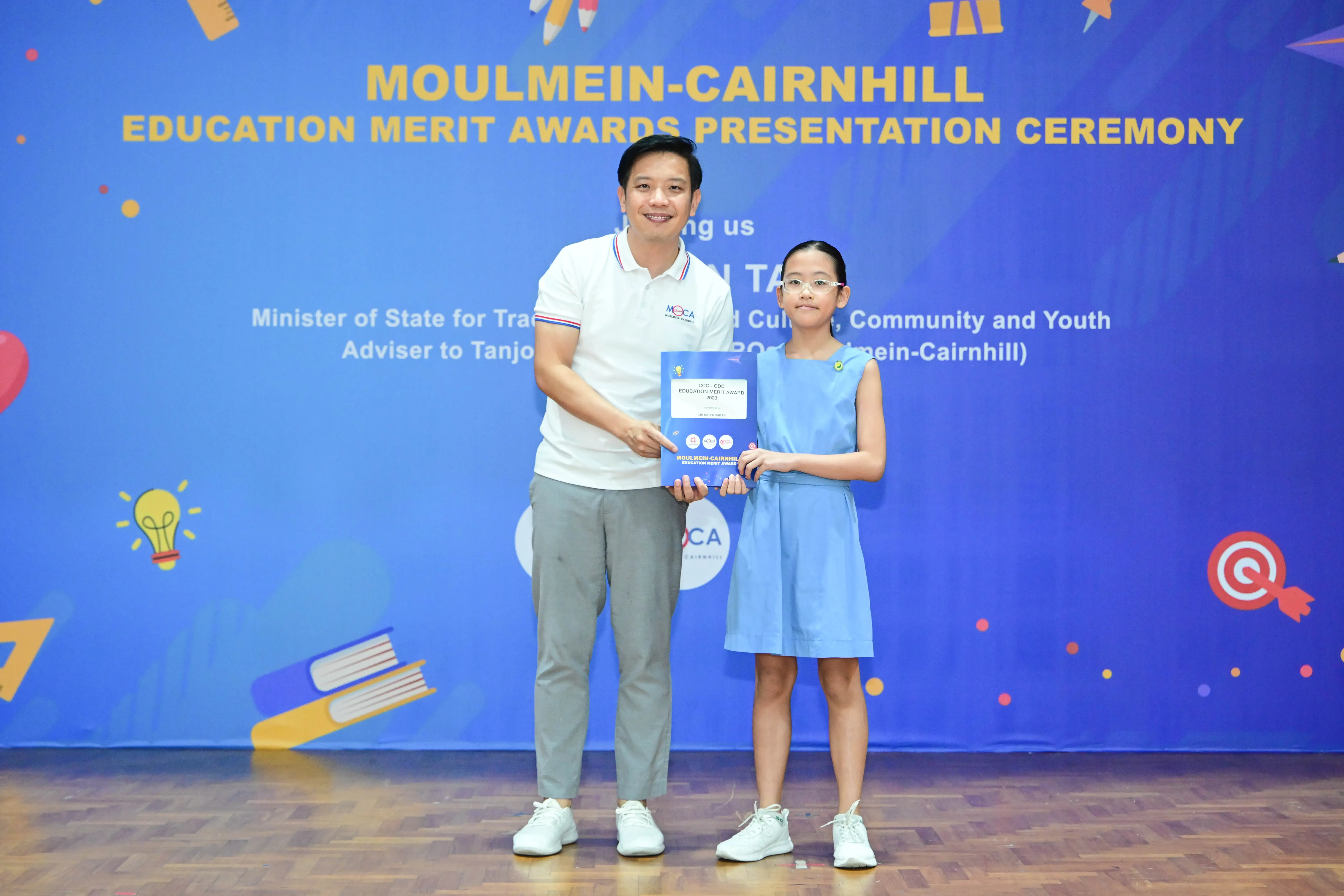 A man and a young girl hold an award certificate at the Moulmein-Cairnhill Education Merit Awards Presentation Ceremony.