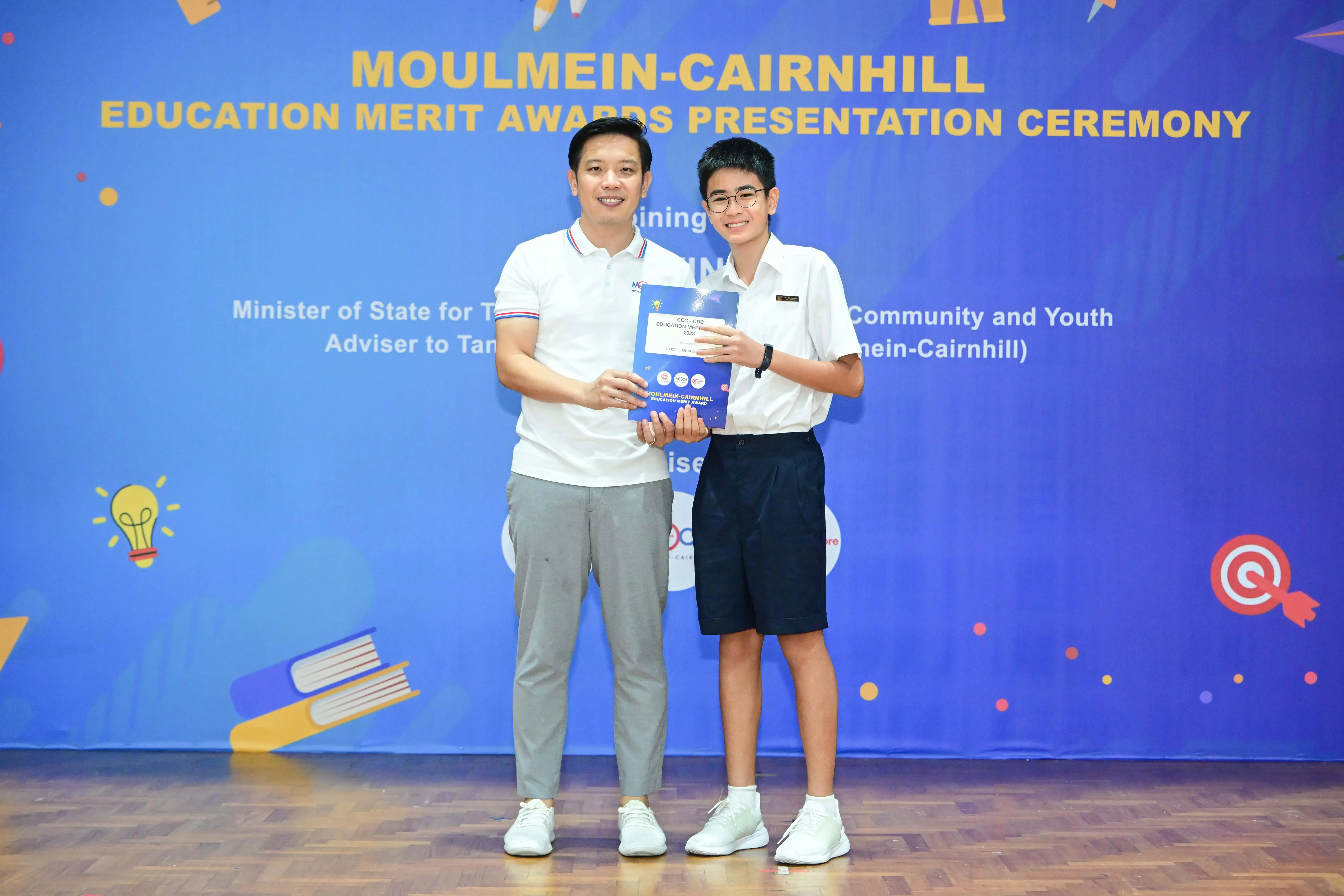 Two people hold an award certificate at the Moulmein-Cairnhill Education Merit Awards Presentation Ceremony.