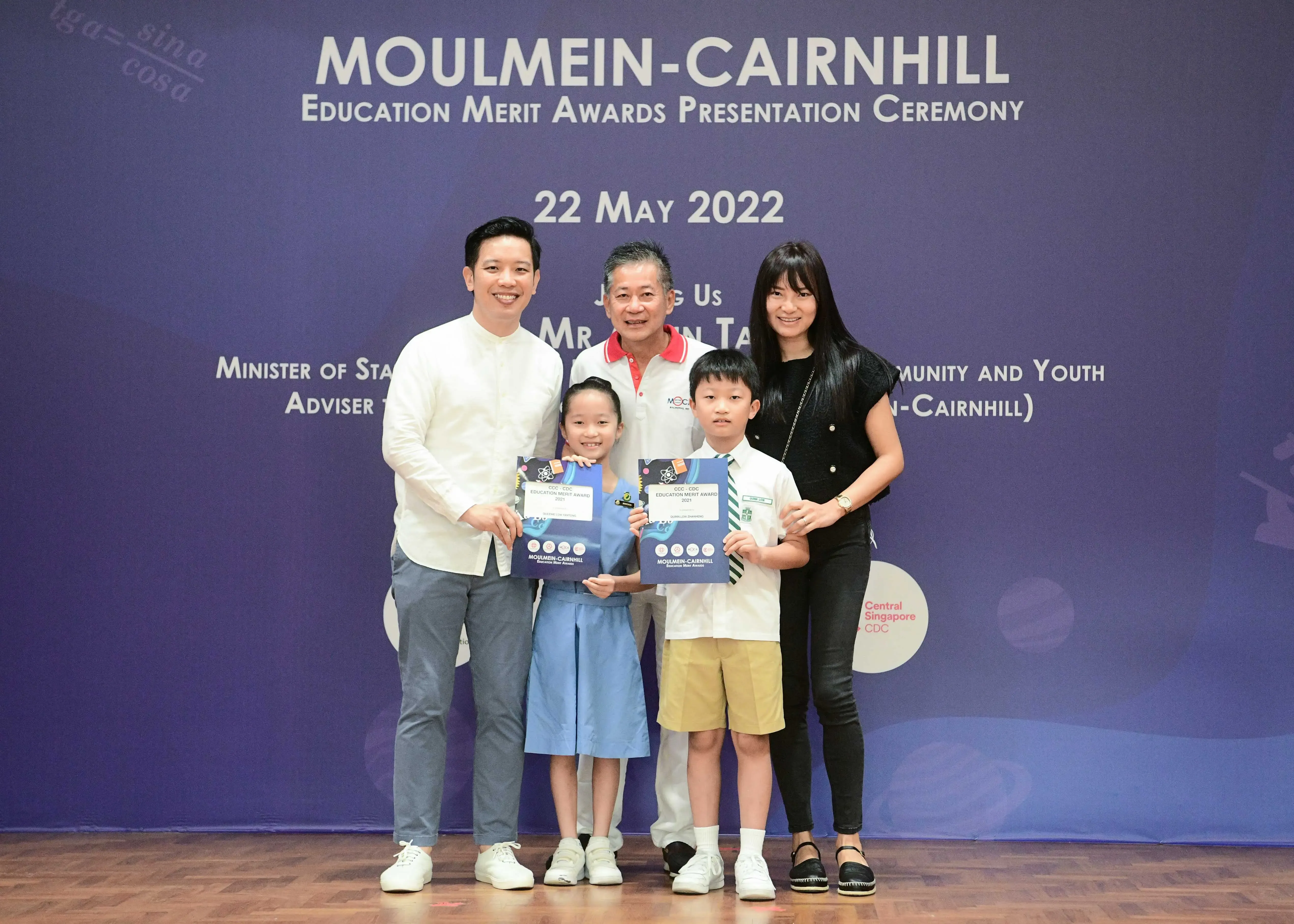 Two children holding merit award certificates pose with three adults at the Moulmein-Cairnhill Education Merit Awards on 22 May 2022.
