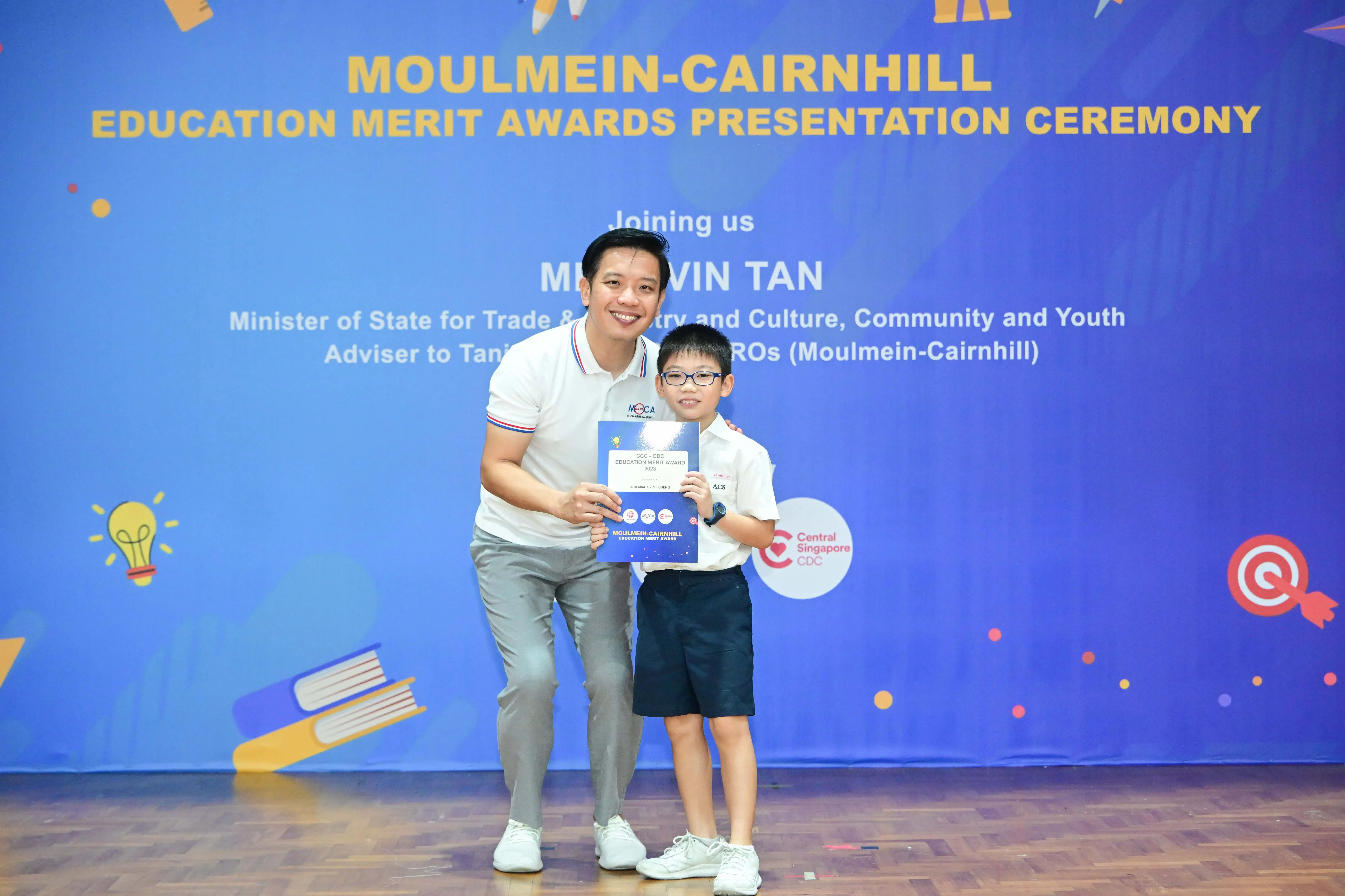 A man and a young boy hold an award certificate at the Moulmein-Cairnhill Education Merit Awards Presentation Ceremony.