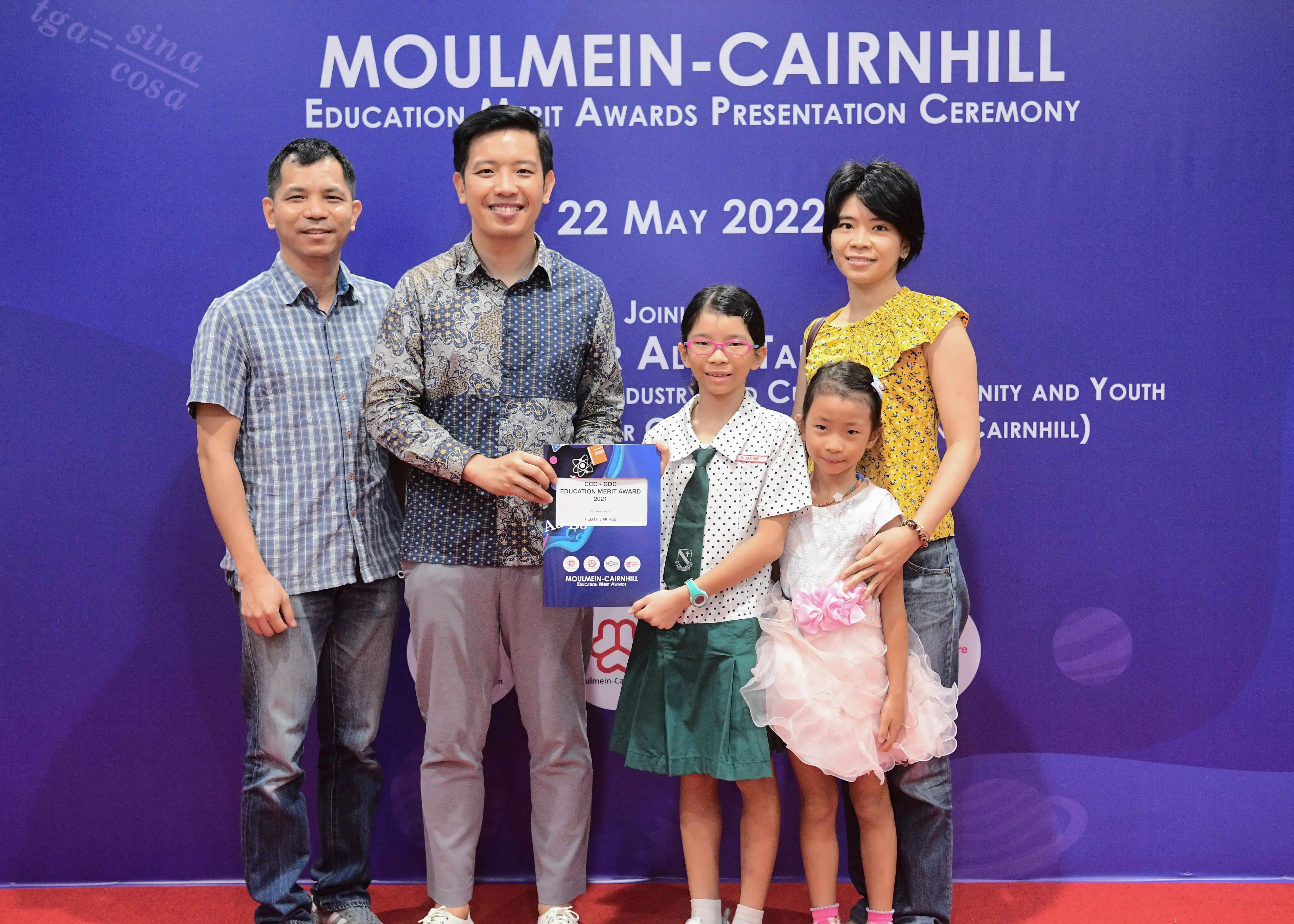 Five people pose at the Moulmein-Cairnhill Education Merit Awards Ceremony on 22 May 2022, holding a blue award certificate.