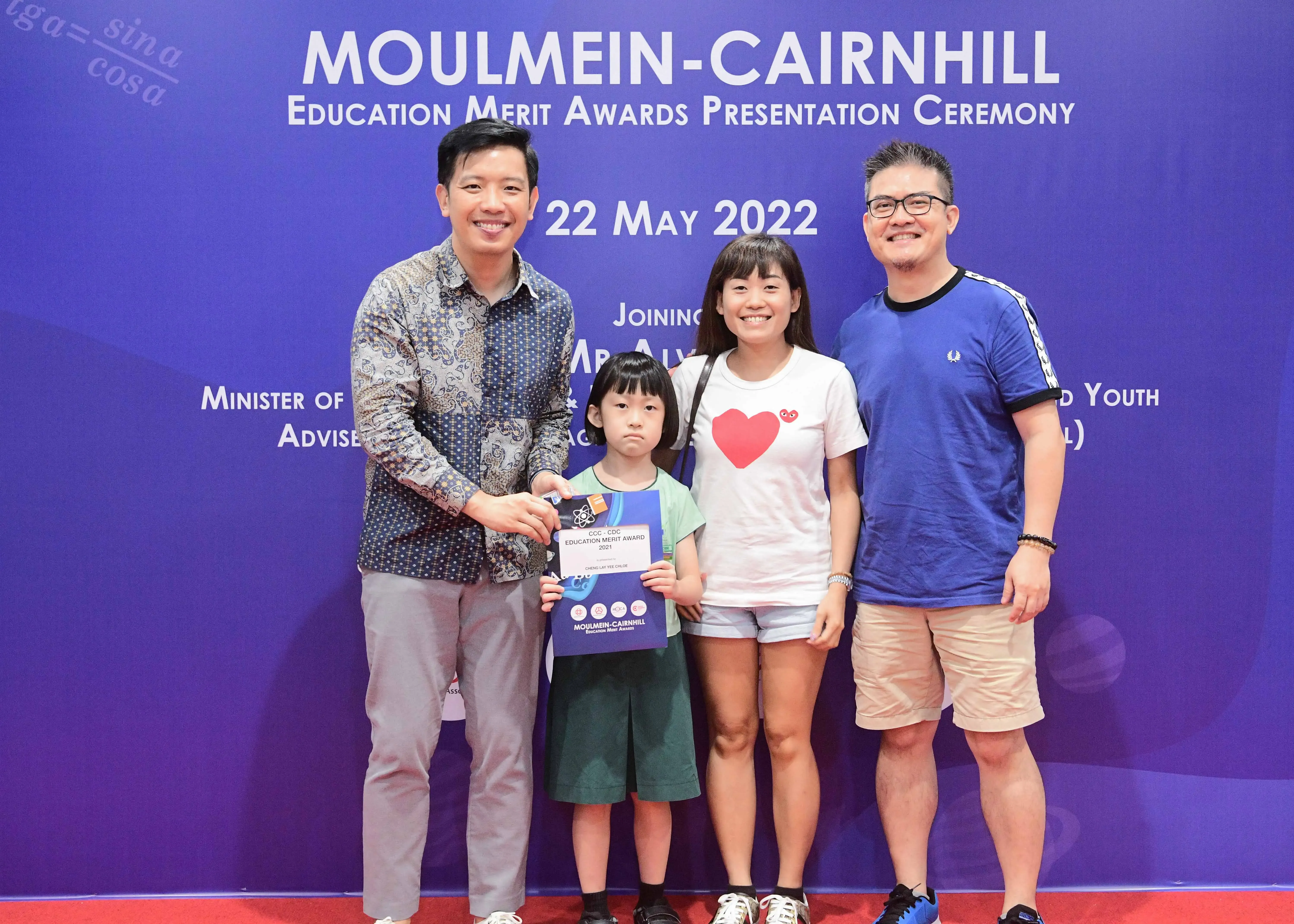 Four people pose at the Moulmein-Cairnhill Education Merit Awards ceremony on 22 May 2022, with a child holding a certificate.