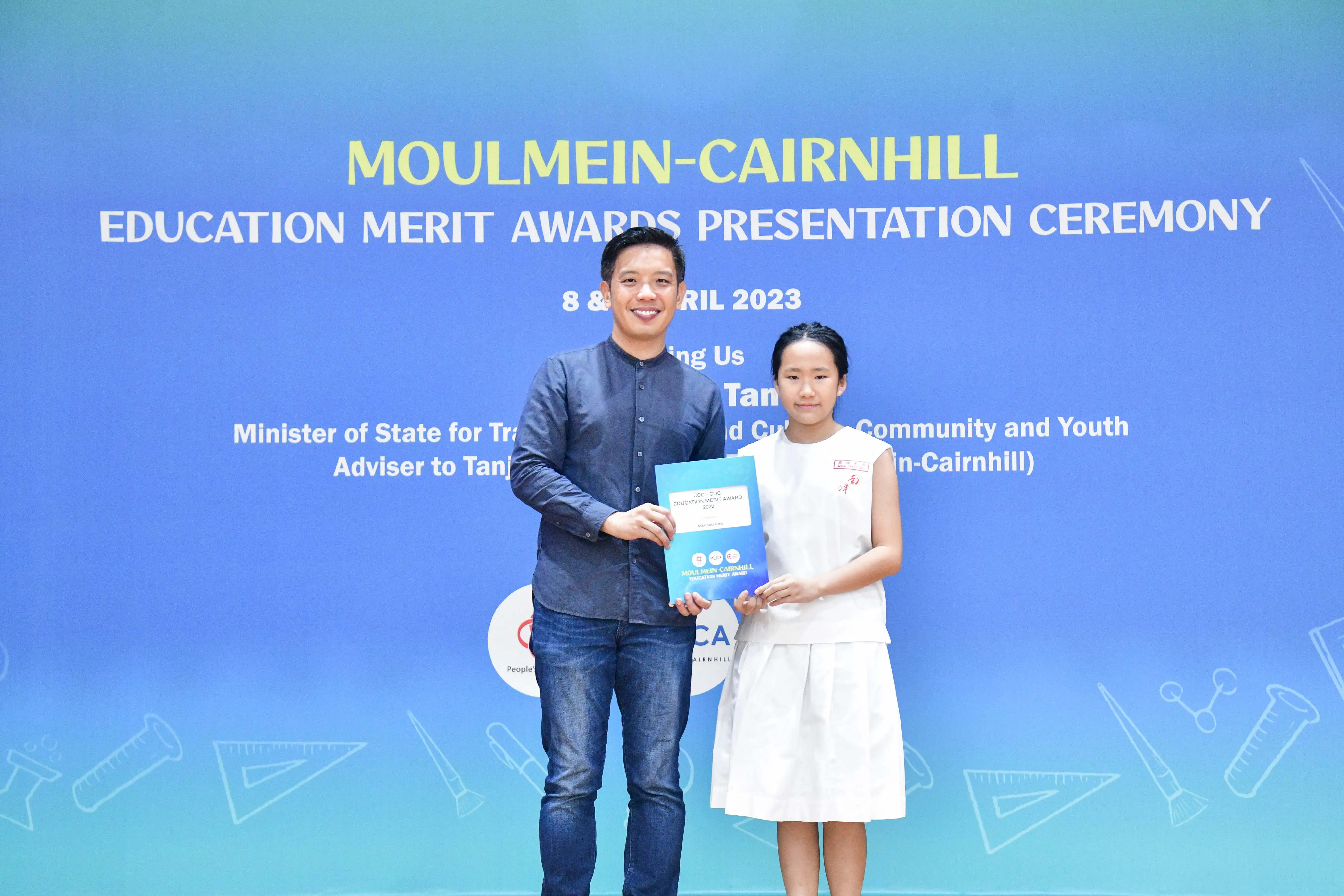 A man and a young girl hold an award certificate at the Moulmein-Cairnhill Education Merit Awards Ceremony, April 2023.