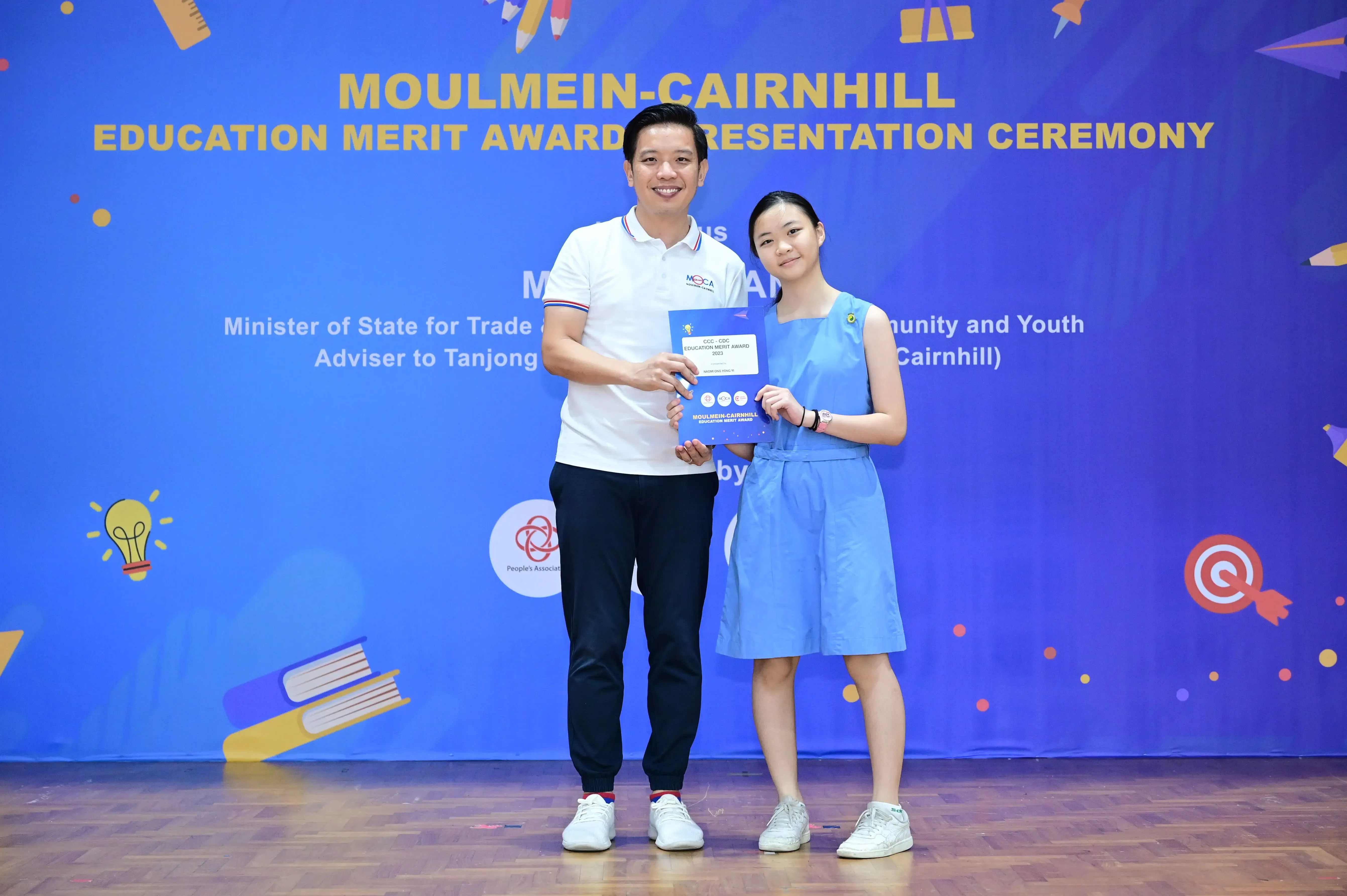 Two people holding a certificate together at the Moulmein-Cairnhill Education Merit Award Presentation Ceremony.