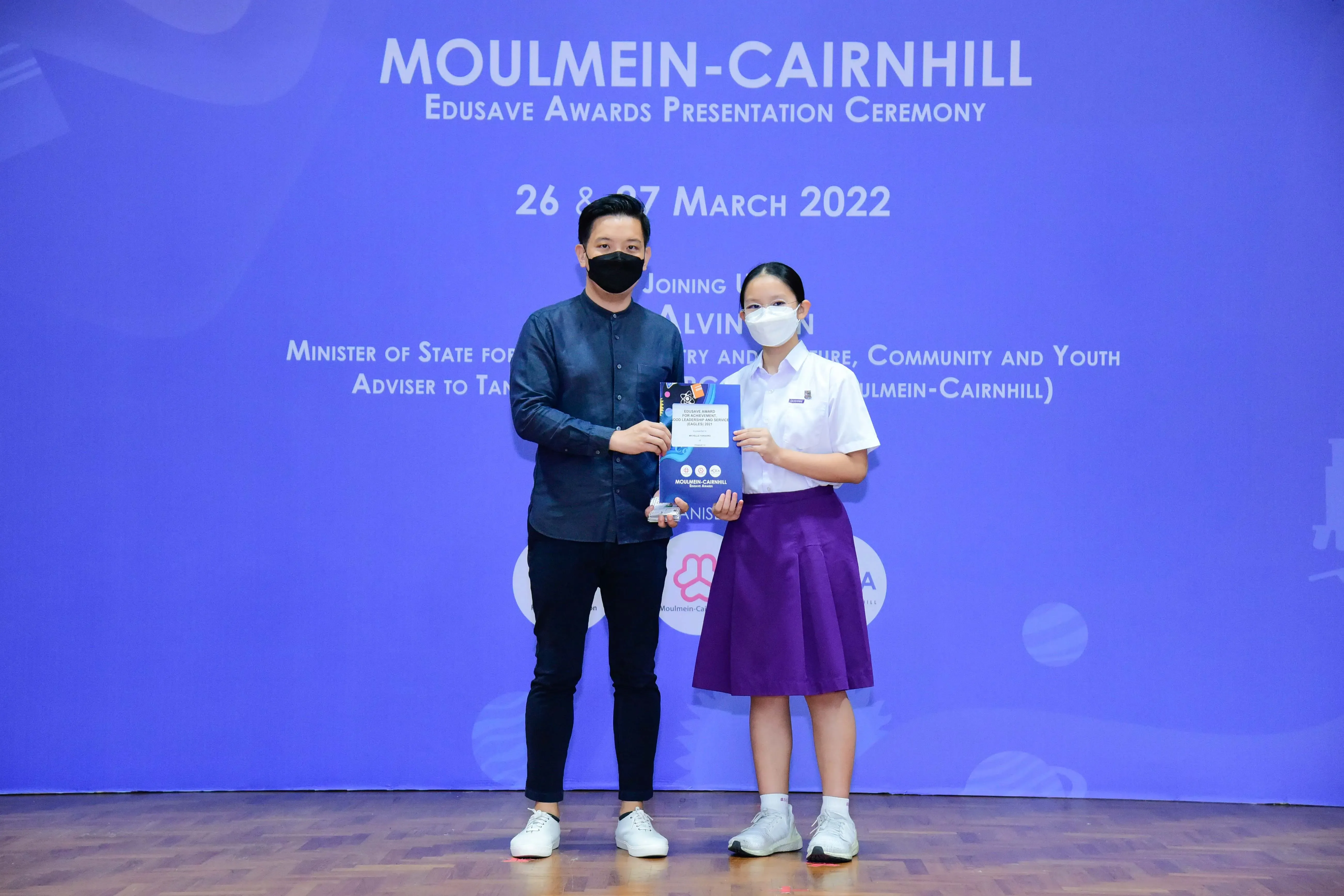 Man and young girl in school uniform hold an award at Moulmein-Cairnhill Edusave Awards Ceremony, March 2022.