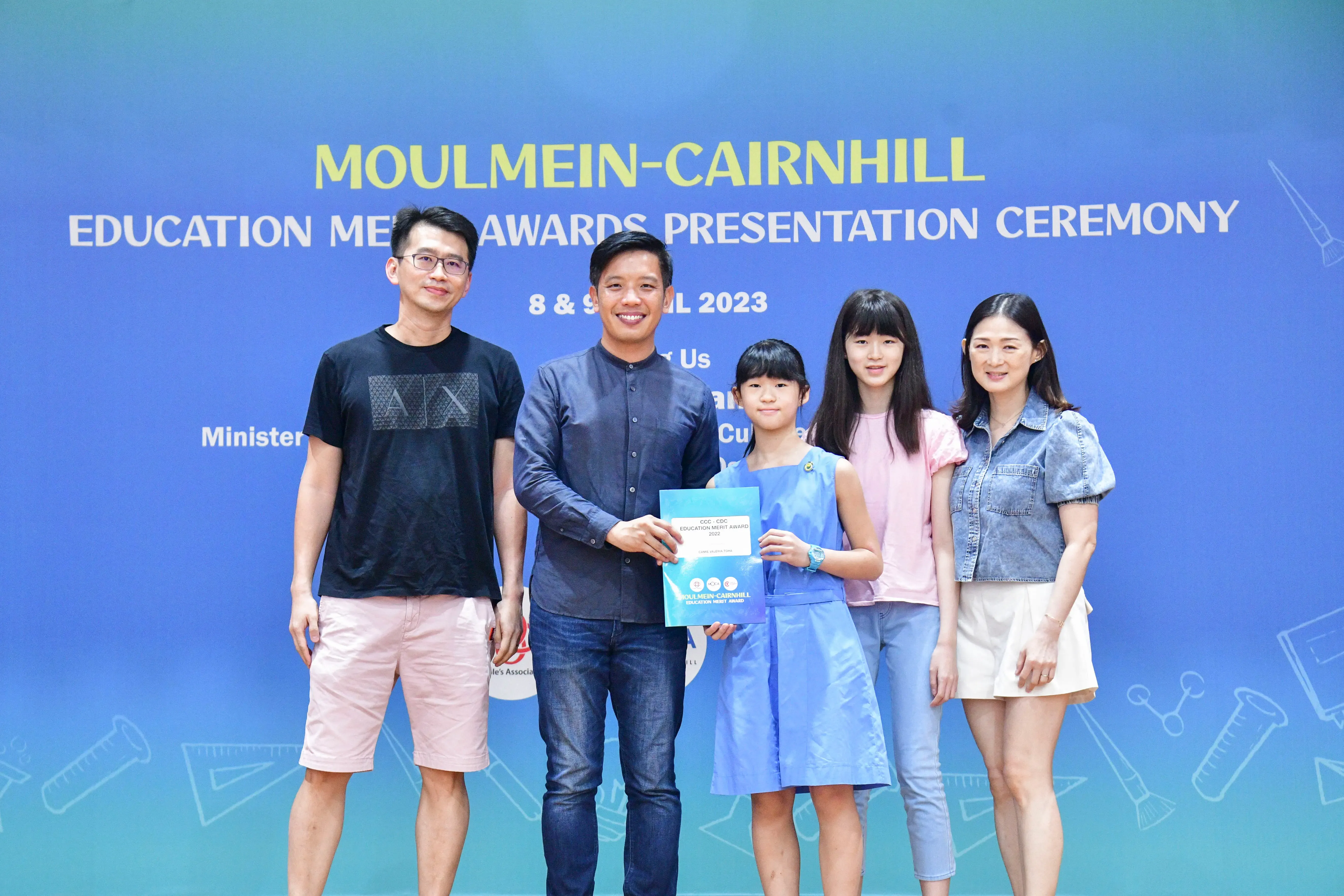 Five people pose at the Moulmein-Cairnhill Education Merit Awards Presentation Ceremony 2023, with a child holding an award.