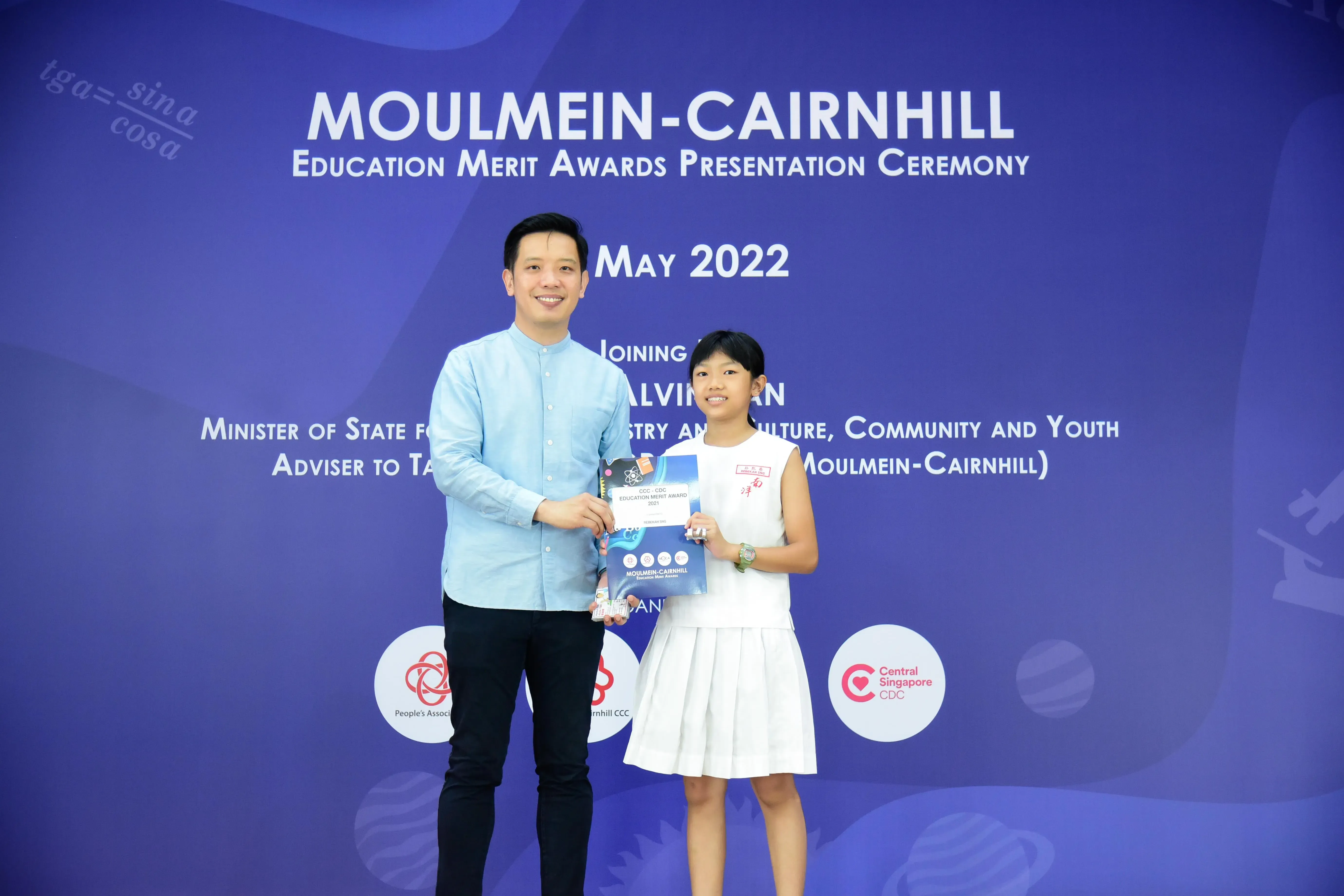 A man and a young girl hold an award booklet at the Moulmein-Cairnhill Education Merit Awards Ceremony, May 2022.