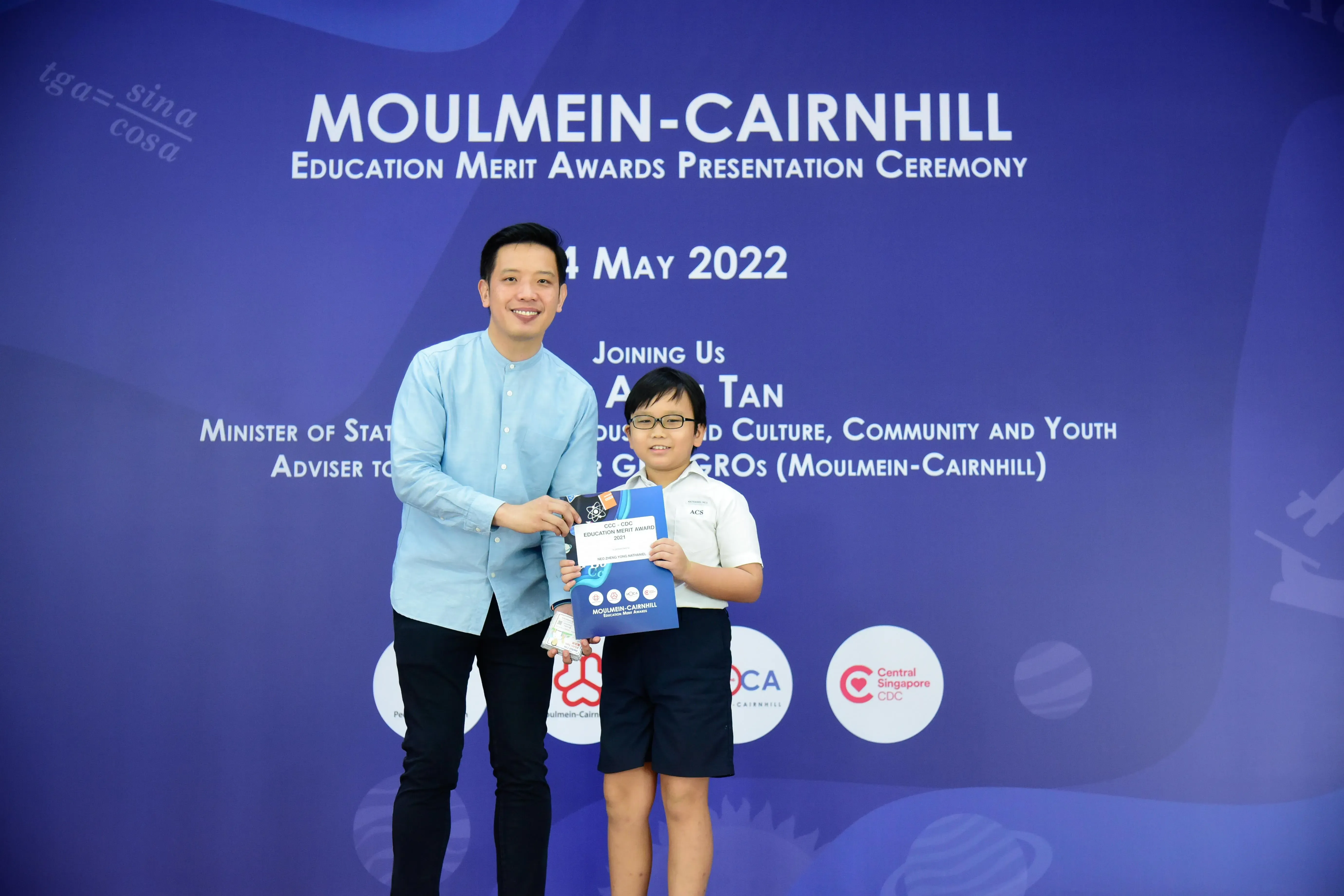 A man and a young boy hold an award certificate at the Moulmein-Cairnhill Education Merit Awards Ceremony, May 2022.