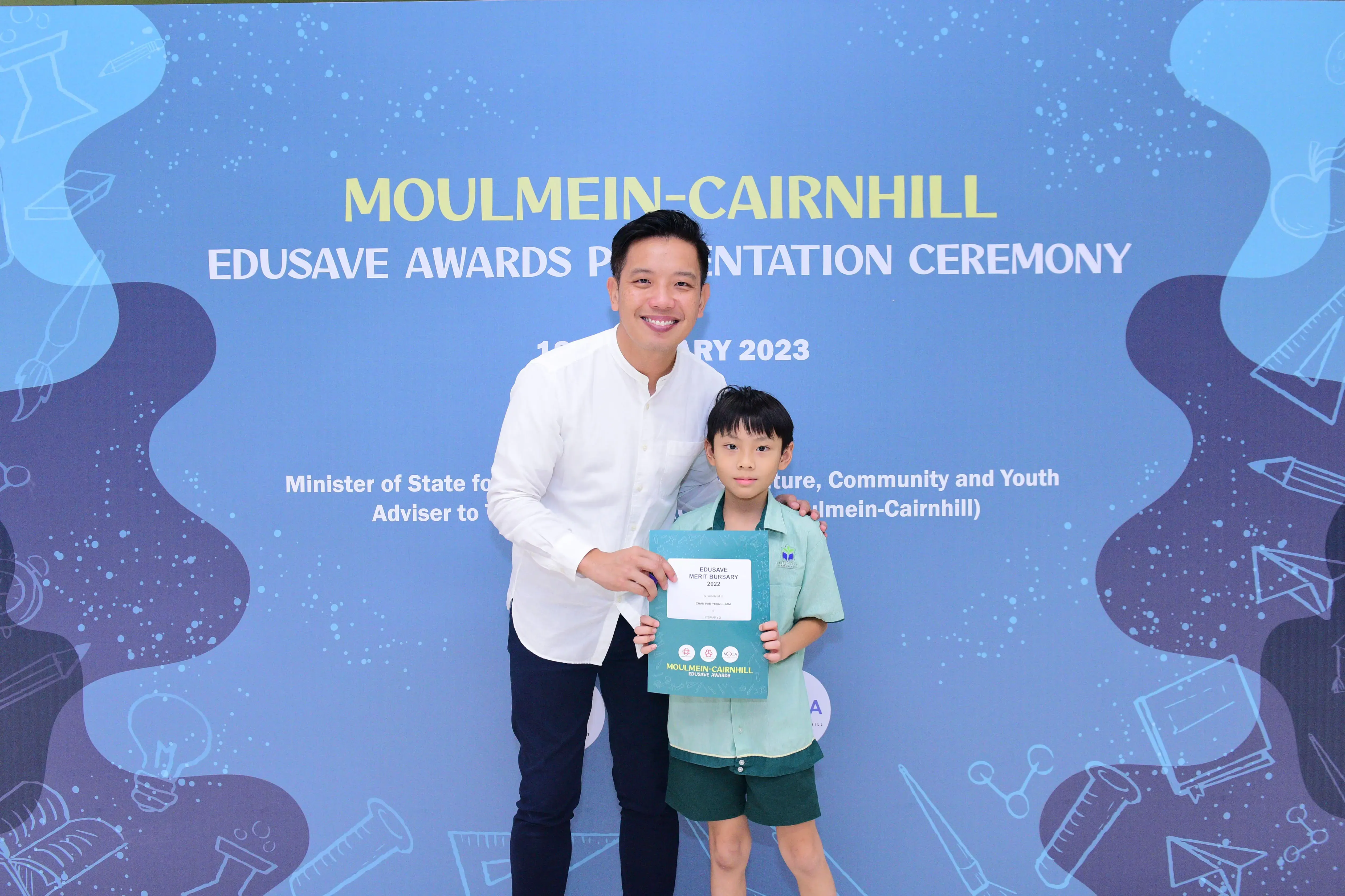 A man and a young boy hold an Edusave Merit Bursary certificate at the 2023 Moulmein-Cairnhill awards ceremony.