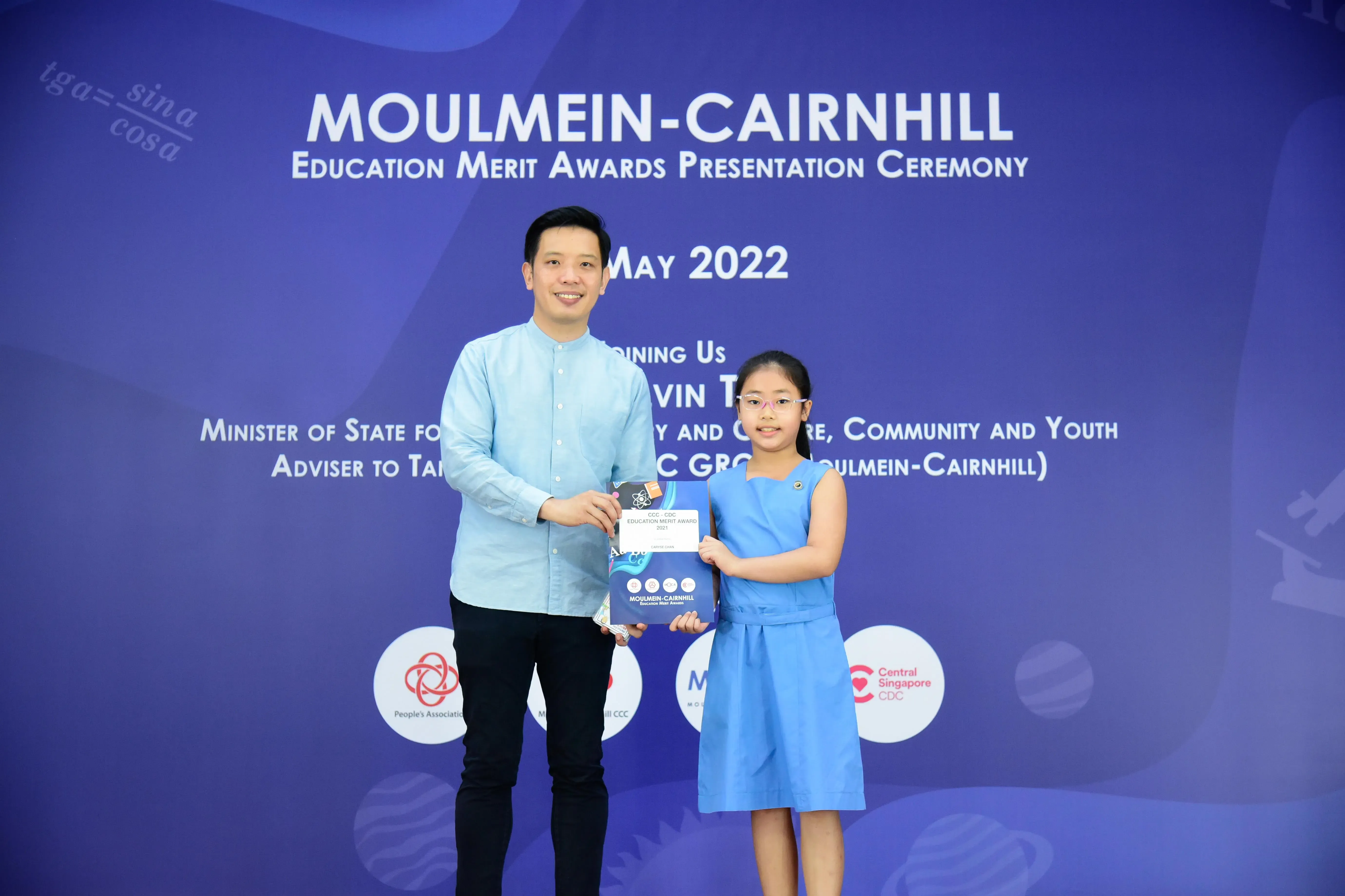 A man and a young girl hold an award together at the Moulmein-Cairnhill Education Merit Awards Ceremony, May 2022.