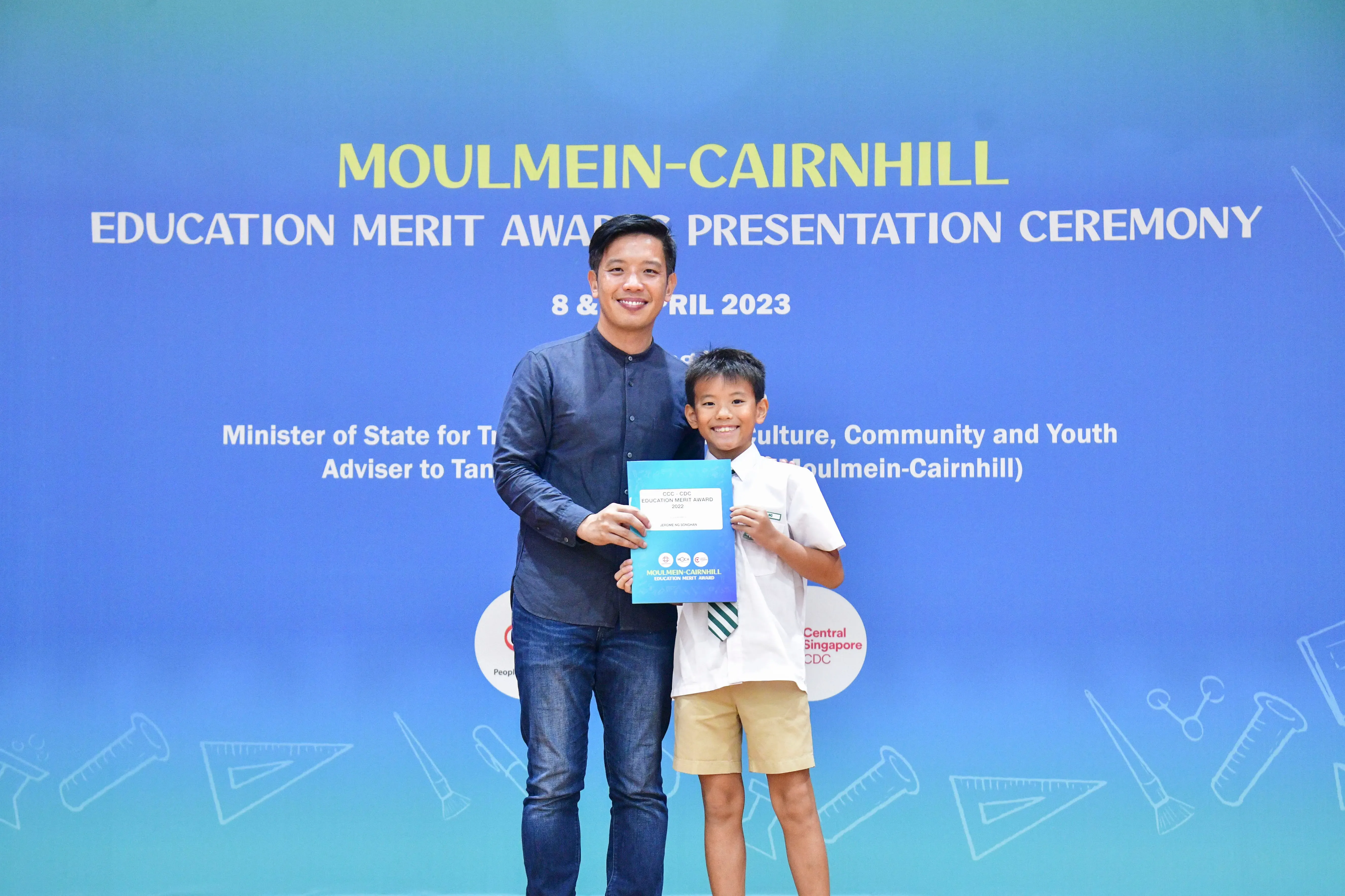 A man and a young boy hold a certificate together at the Moulmein-Cairnhill Education Merit Award Ceremony, April 2023.