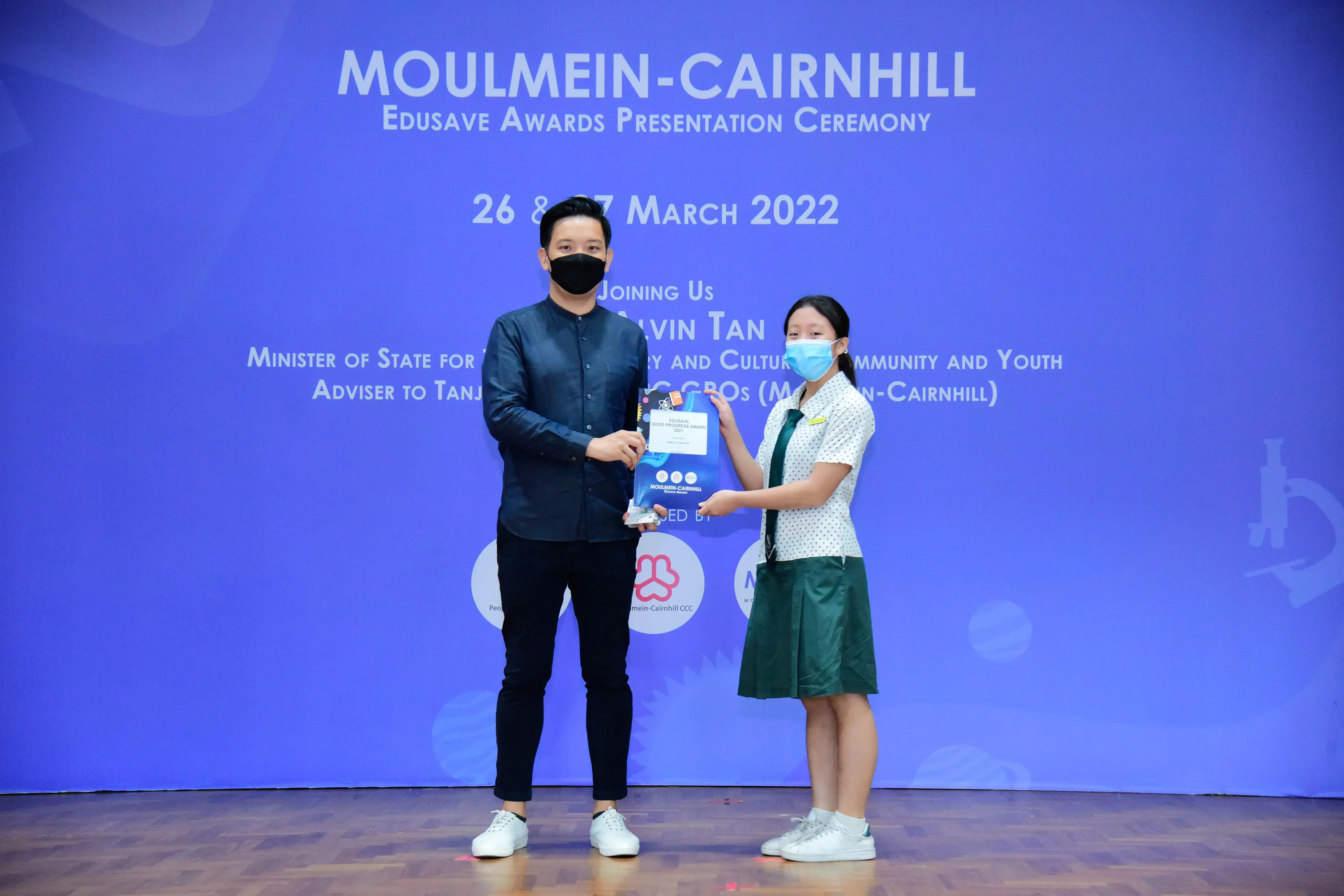 A man and a student in school uniform present an award on stage at the Moulmein-Cairnhill Edusave Awards Ceremony.