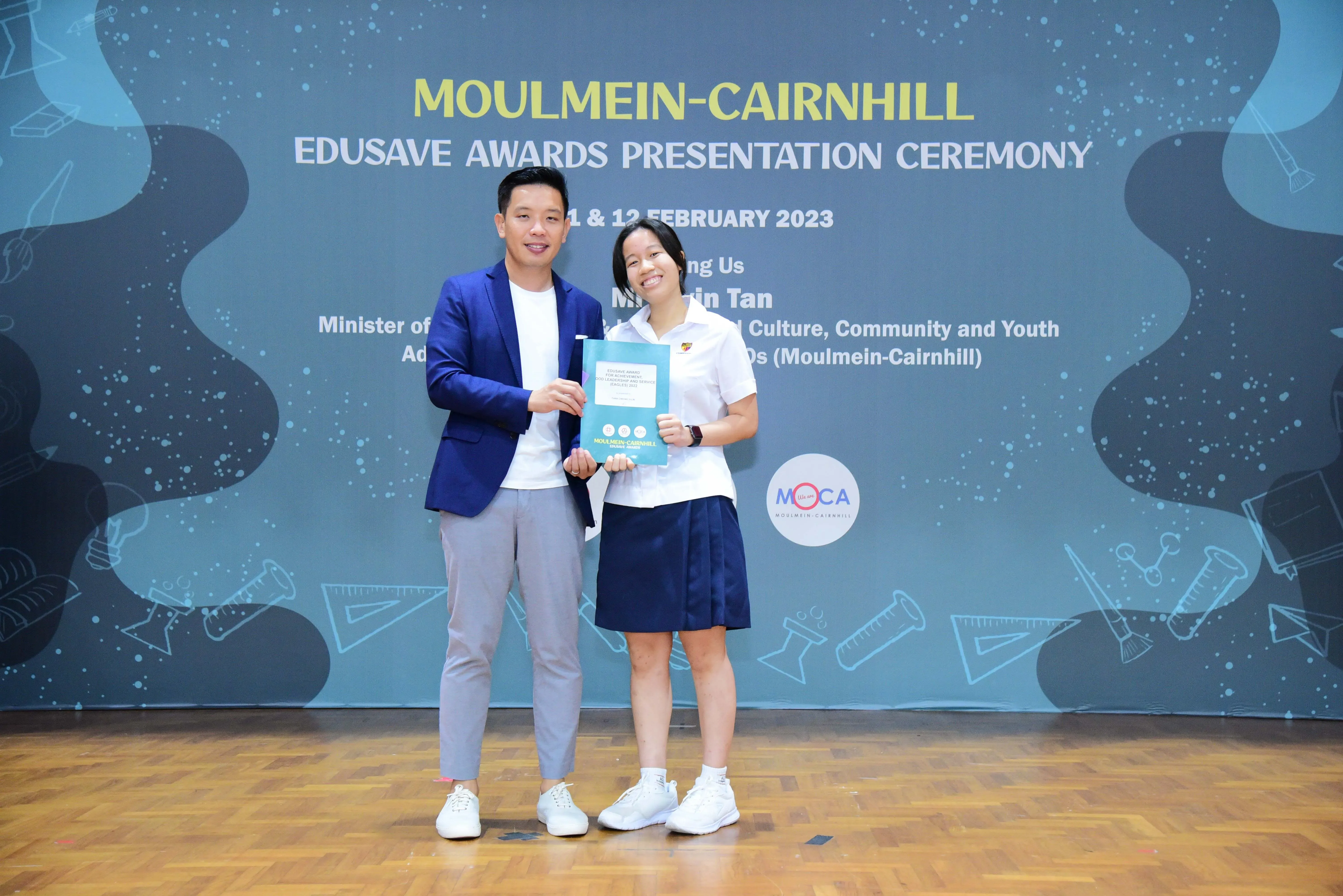 Two people smile holding a certificate at the Moulmein-Cairnhill Edusave Awards Presentation Ceremony, February 2023.