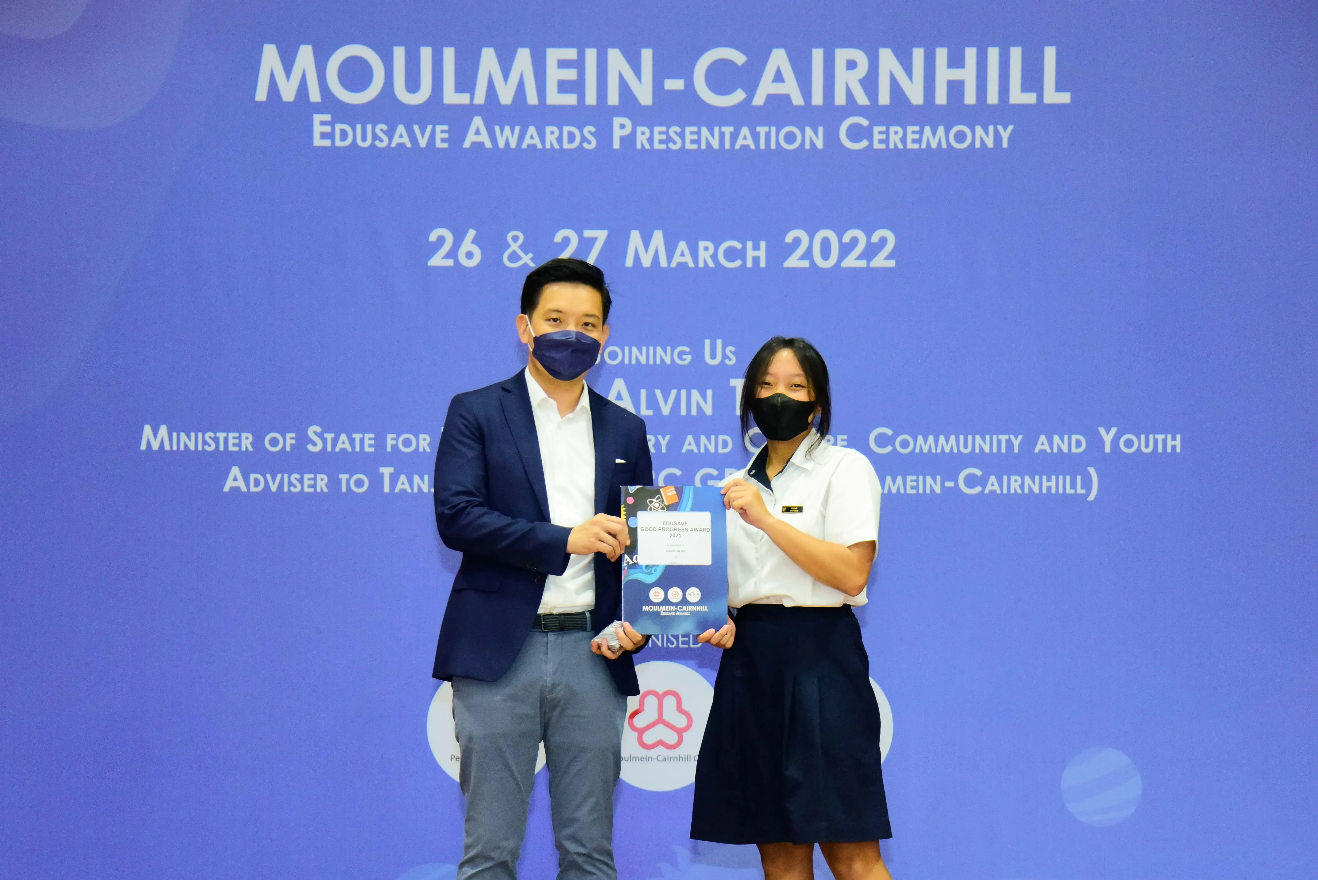 Two masked people hold an award certificate at the Moulmein-Cairnhill Edusave Awards Ceremony, March 2022.