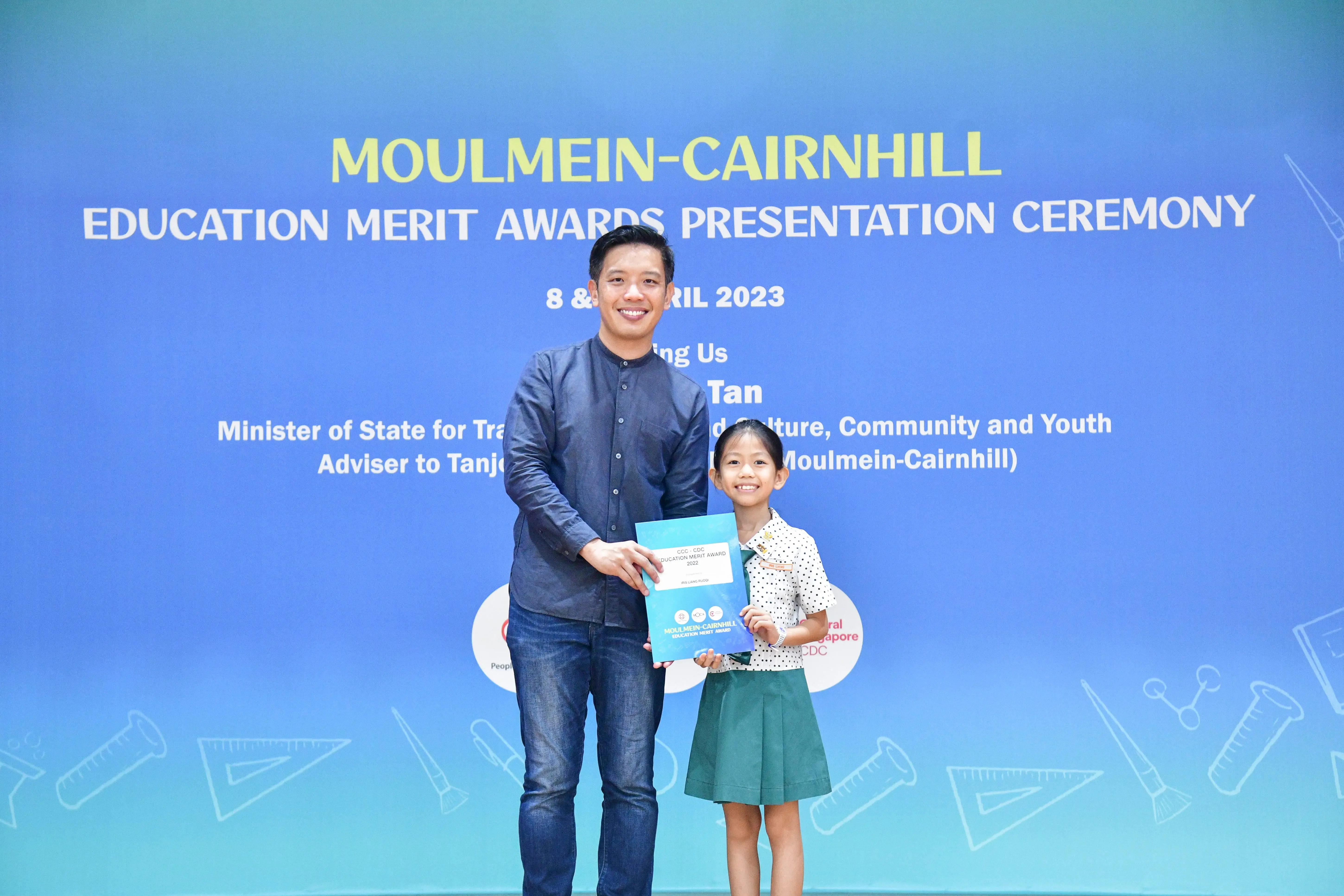 A man and a young girl hold a certificate together at the Moulmein-Cairnhill Education Merit Awards Ceremony, April 2023.