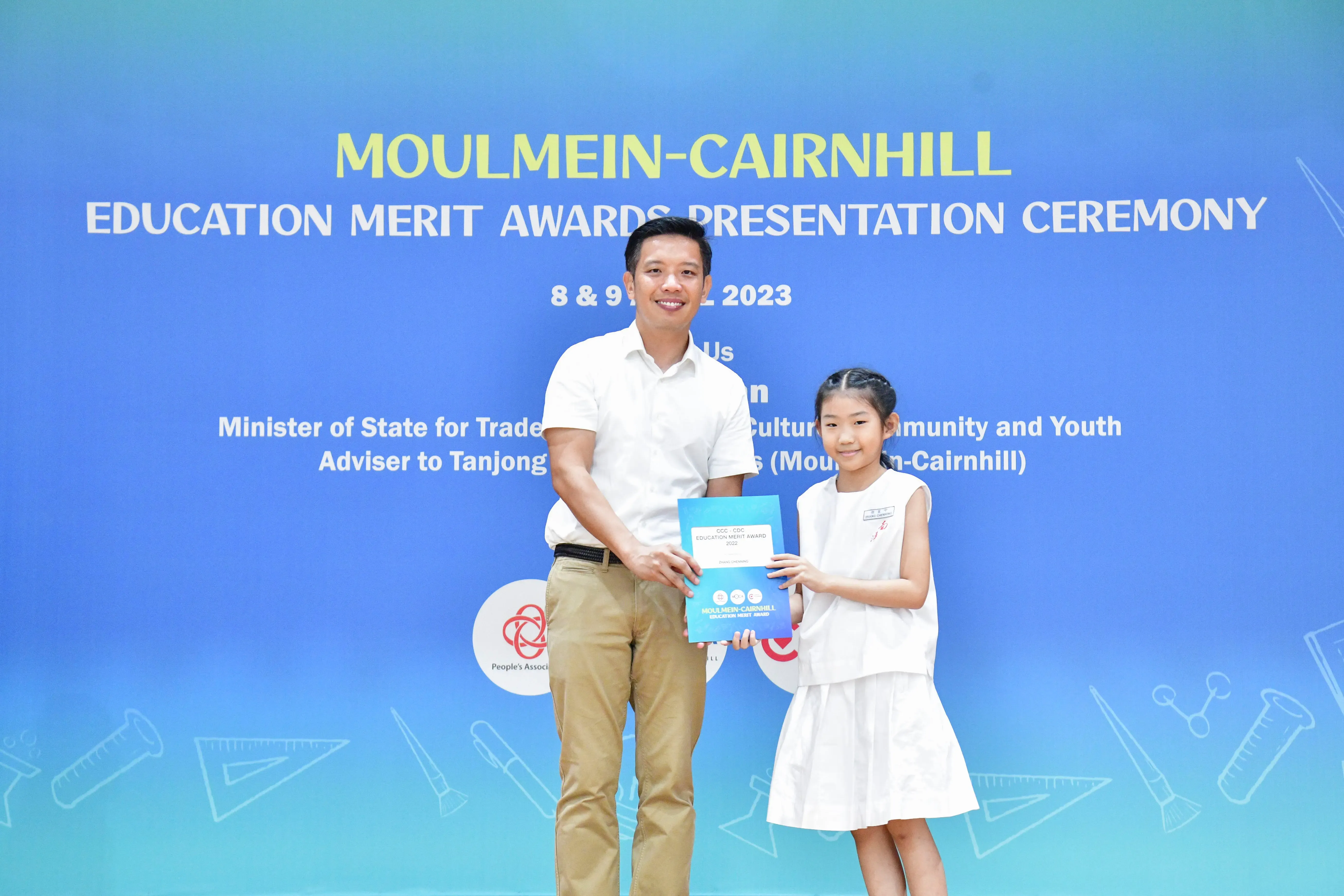 A man and a young girl hold a blue certificate together at the Moulmein-Cairnhill Education Merit Awards 2023.