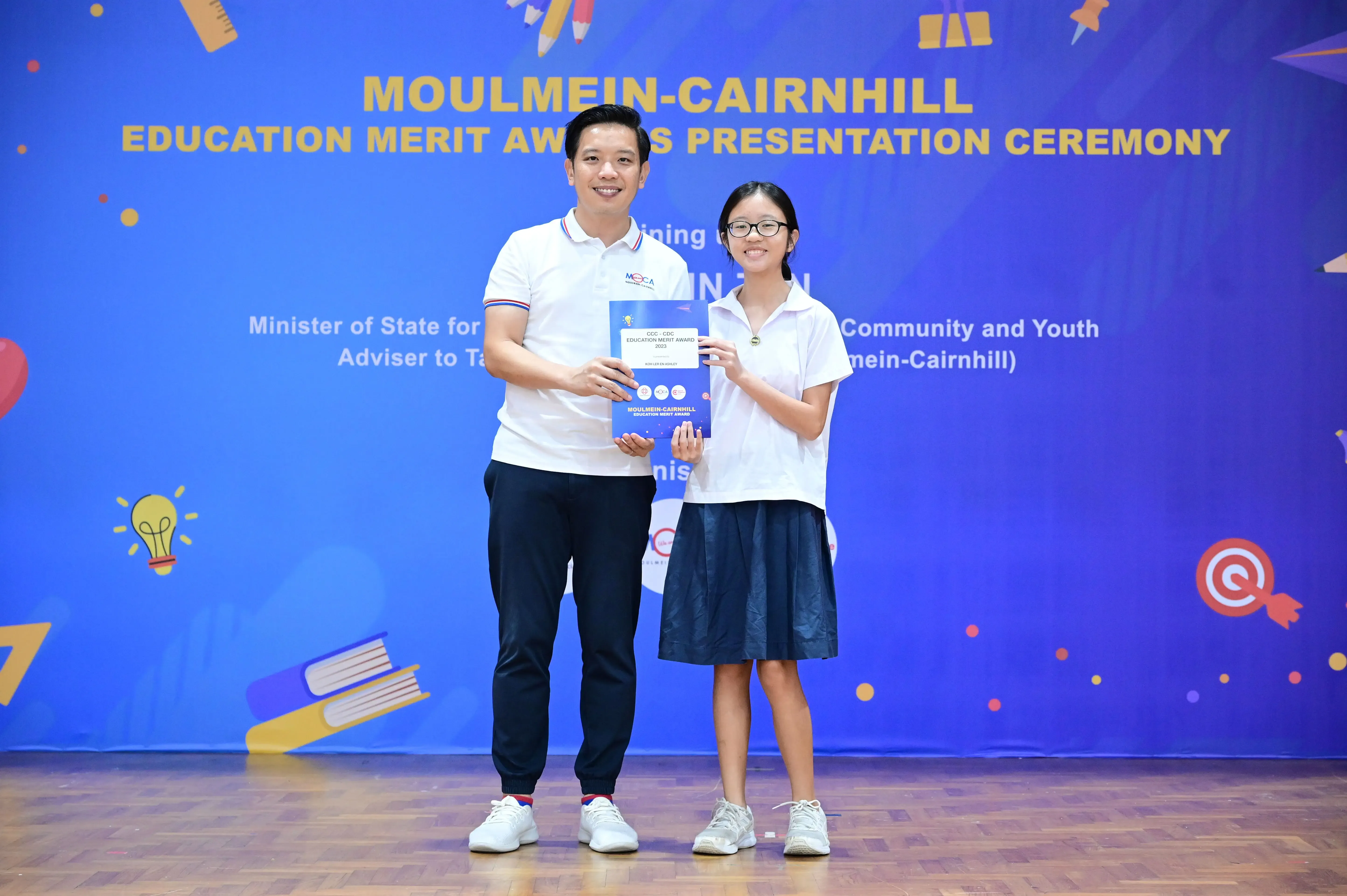 A man and a young girl hold an award certificate at the Moulmein-Cairnhill Education Merit Awards Presentation Ceremony.