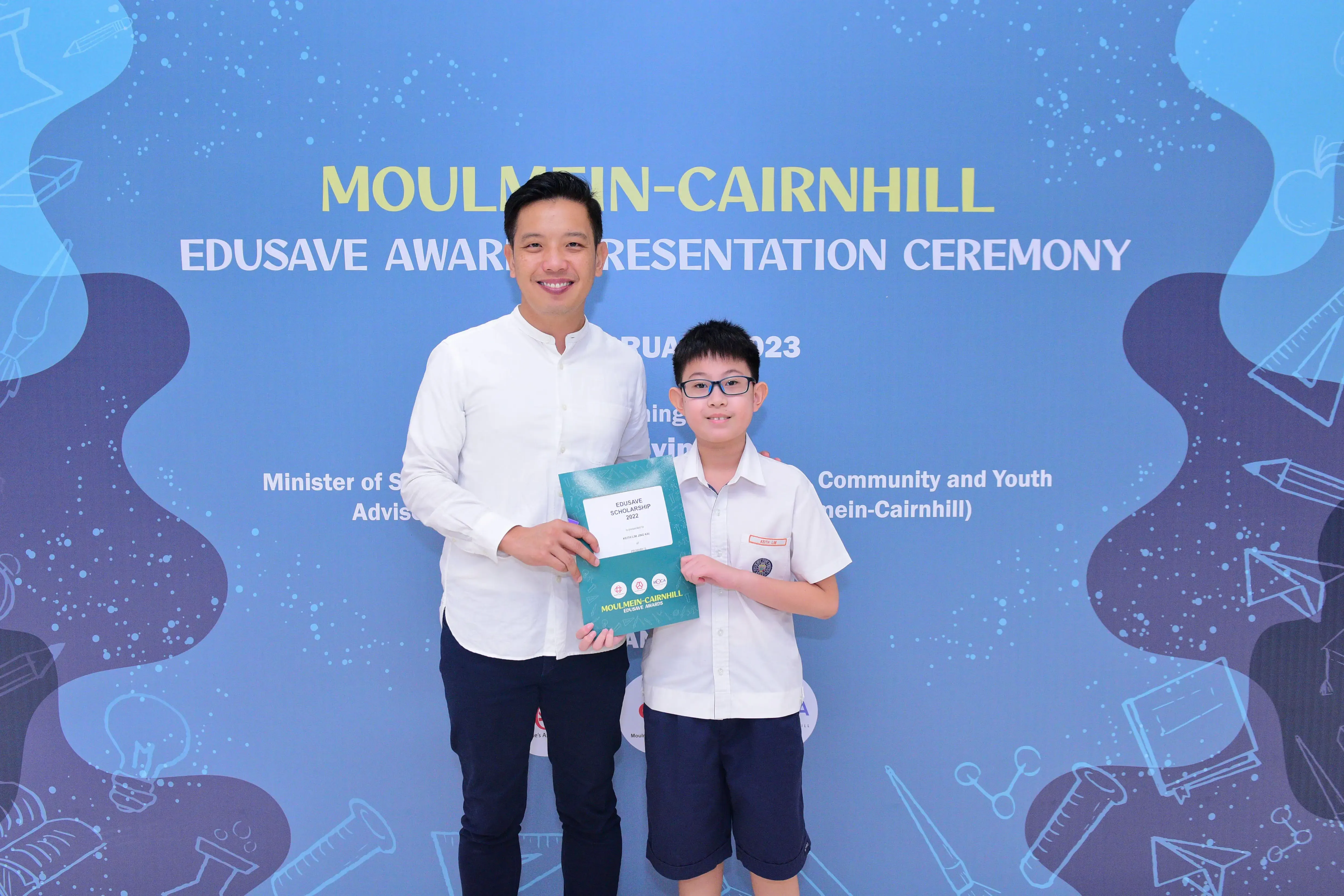 A man and a young boy holding an Edusave Scholarship booklet at the Moulmein-Cairnhill Edusave Award Presentation Ceremony.