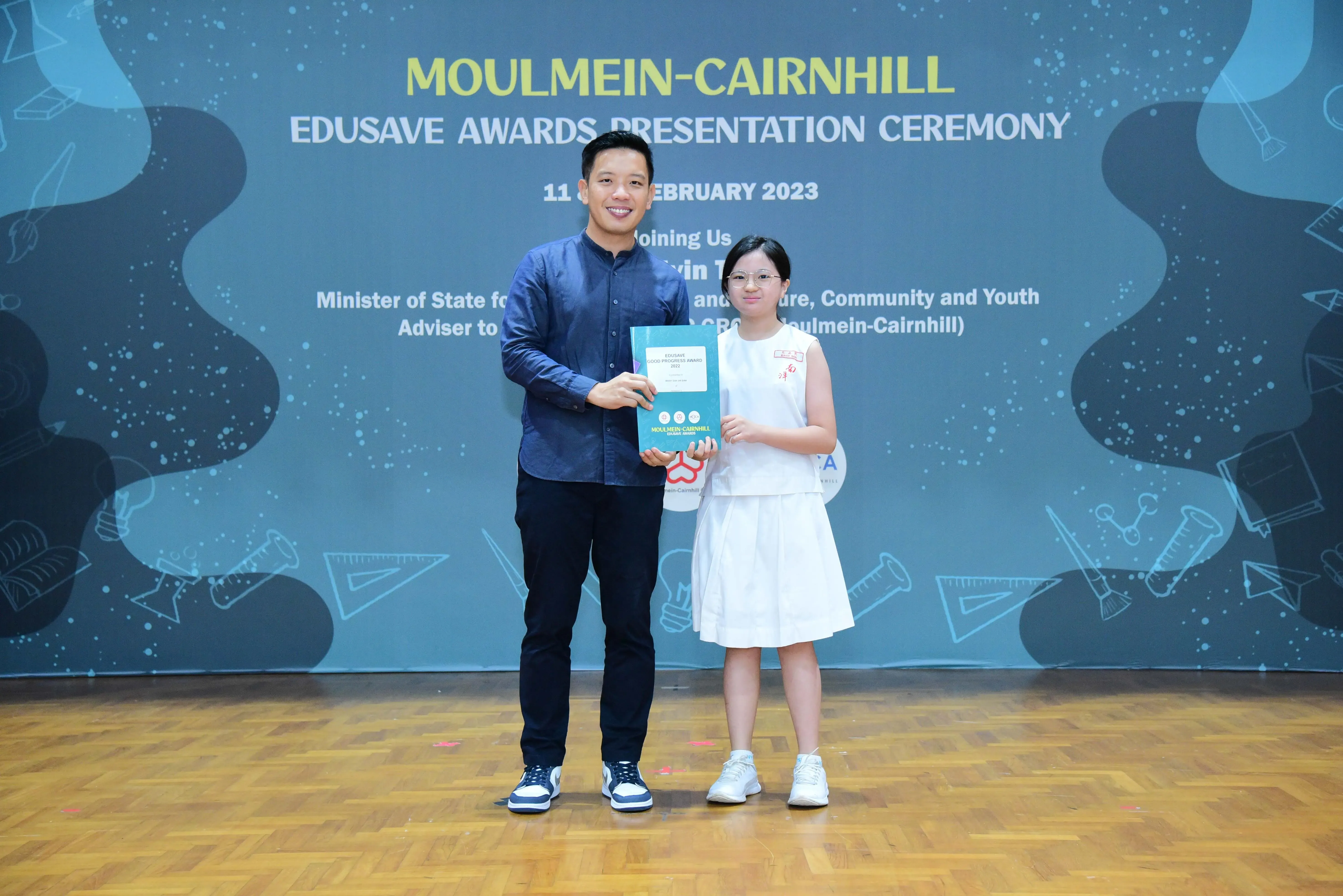 A man and a young girl hold a certificate together at the Moulmein-Cairnhill Edusave Awards Ceremony, February 2023.