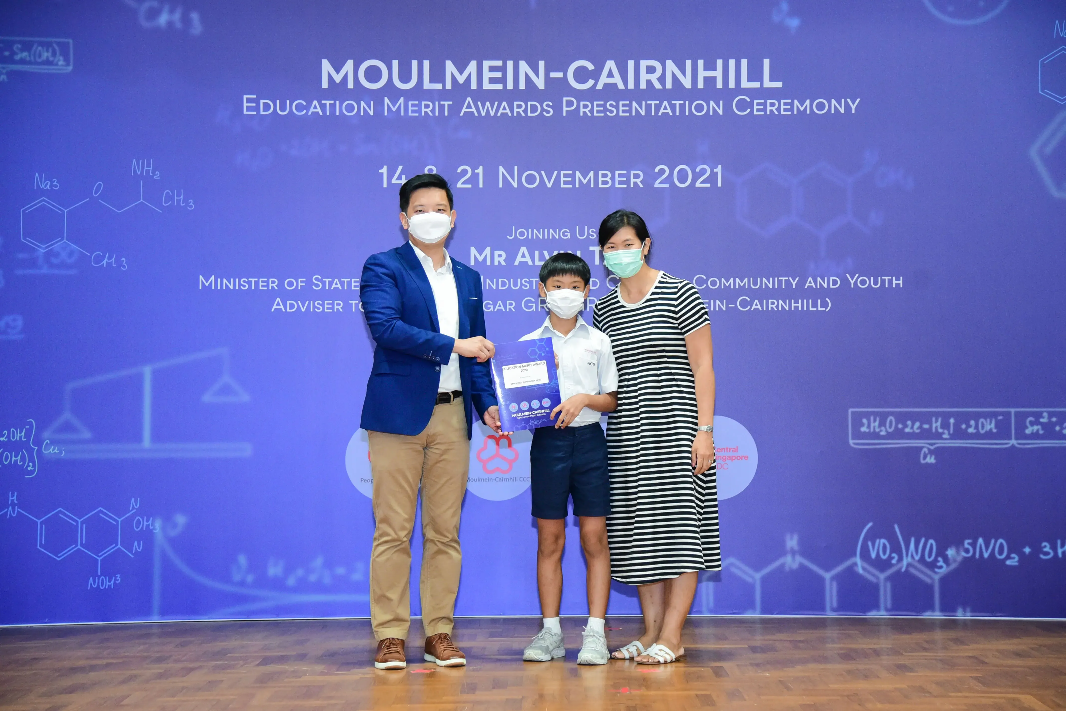 A man, boy, and woman wearing masks pose at the Moulmein-Cairnhill Education Merit Awards Ceremony, November 2021.