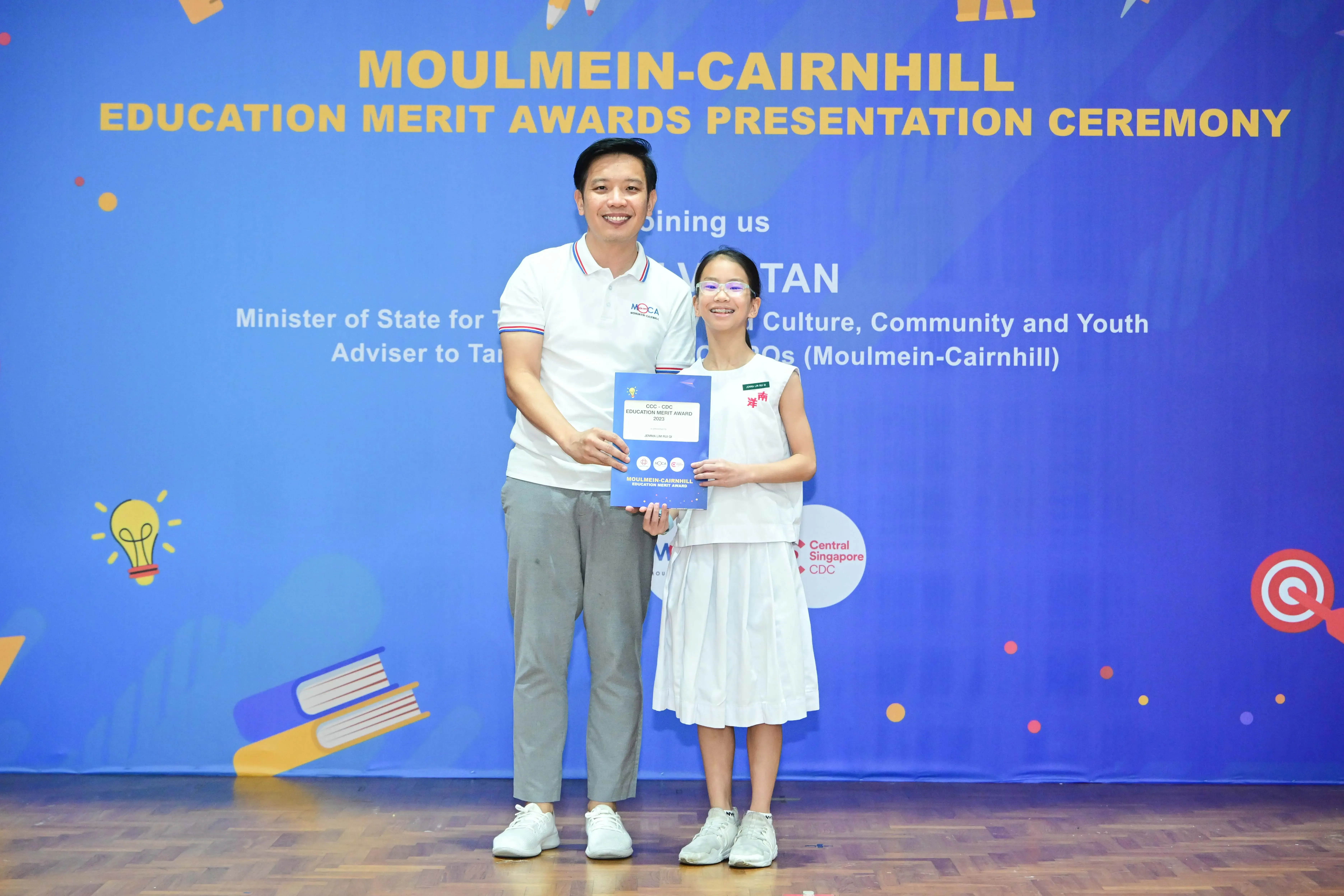 A man and a young girl hold a certificate together at the Moulmein-Cairnhill Education Merit Awards Ceremony.