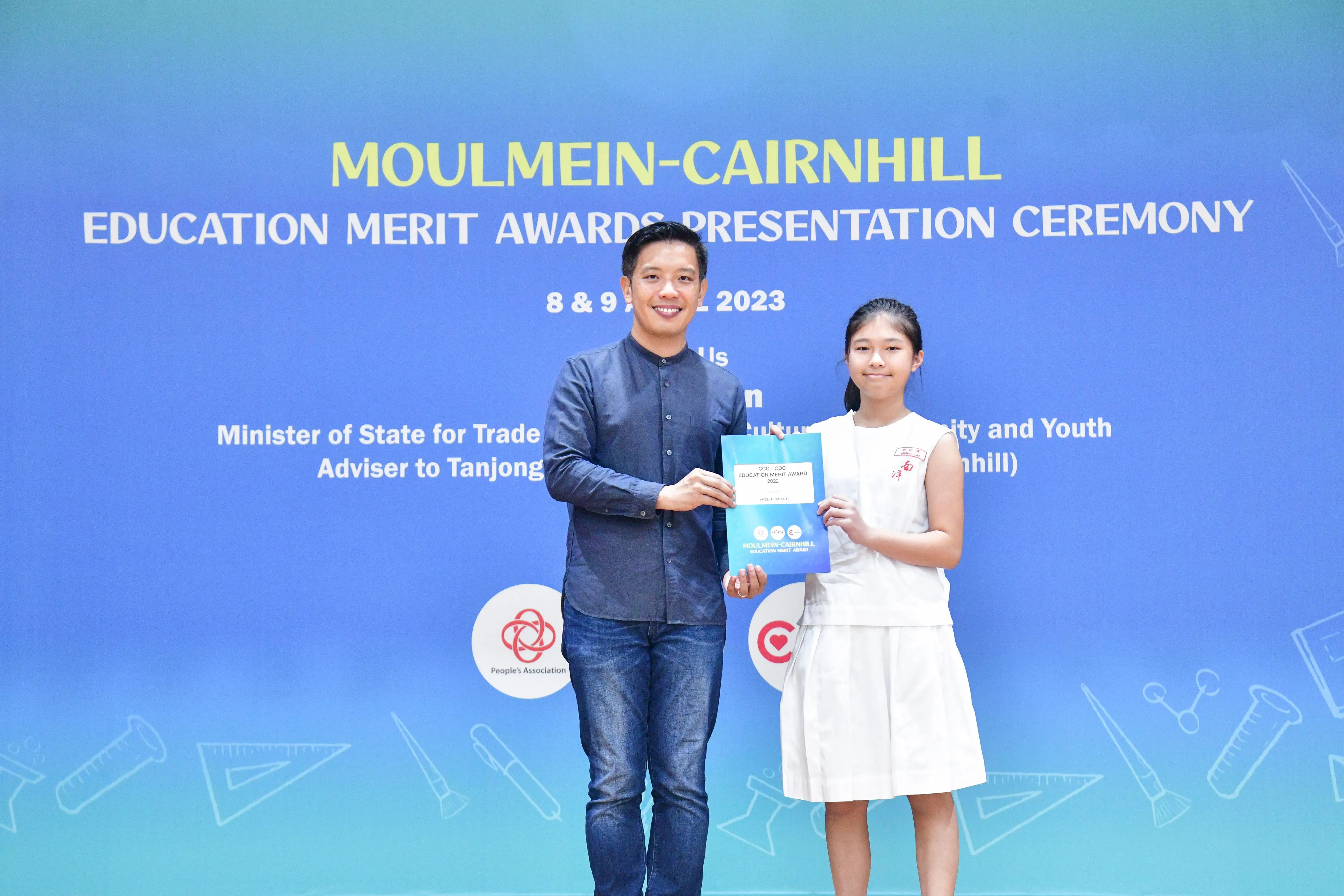A man and a young girl hold an award certificate at the Moulmein-Cairnhill Education Merit Awards Ceremony 2023.