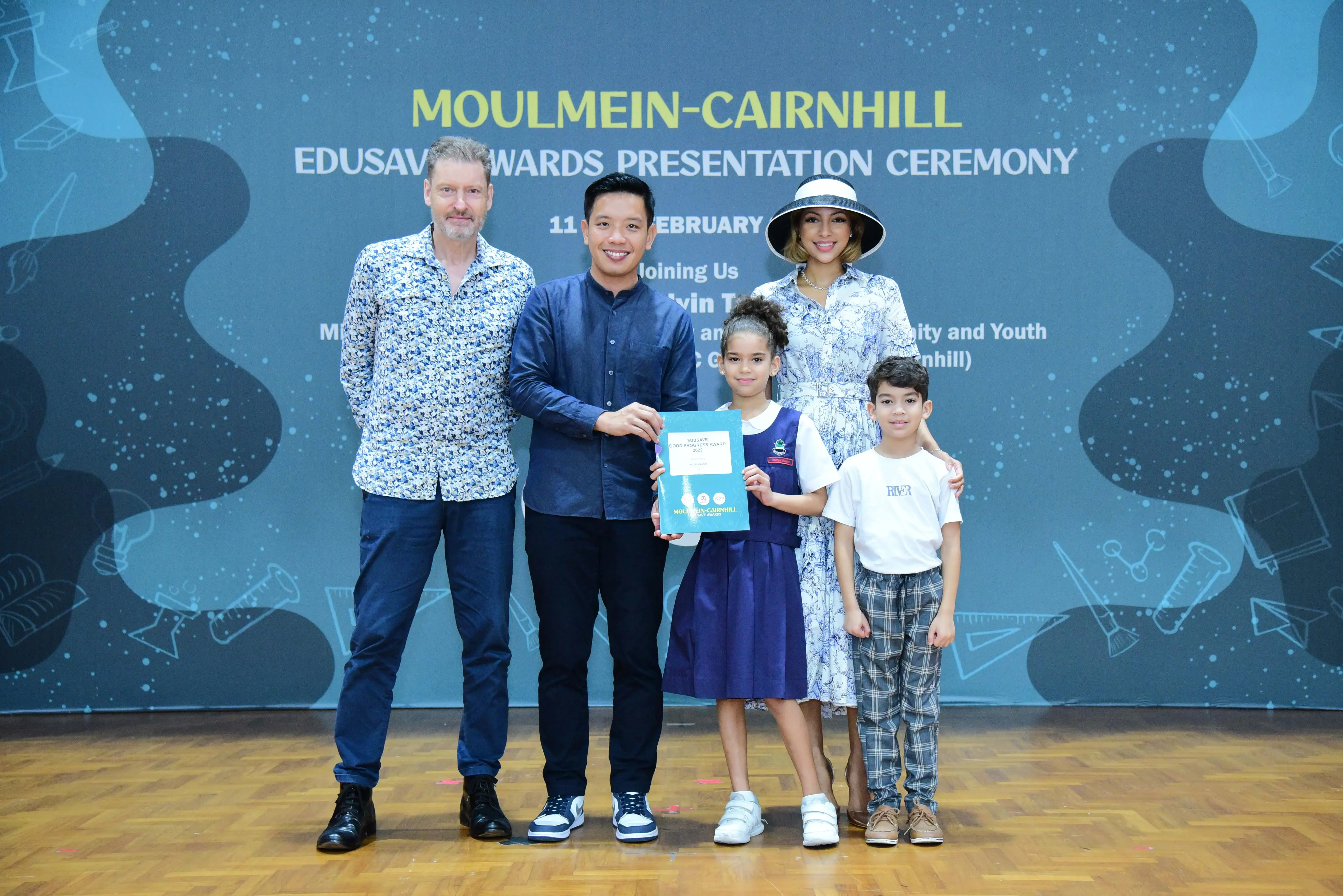 Three adults and two children pose at the Moulmein-Cairnhill Edusave Awards Presentation Ceremony, girl holds a certificate.