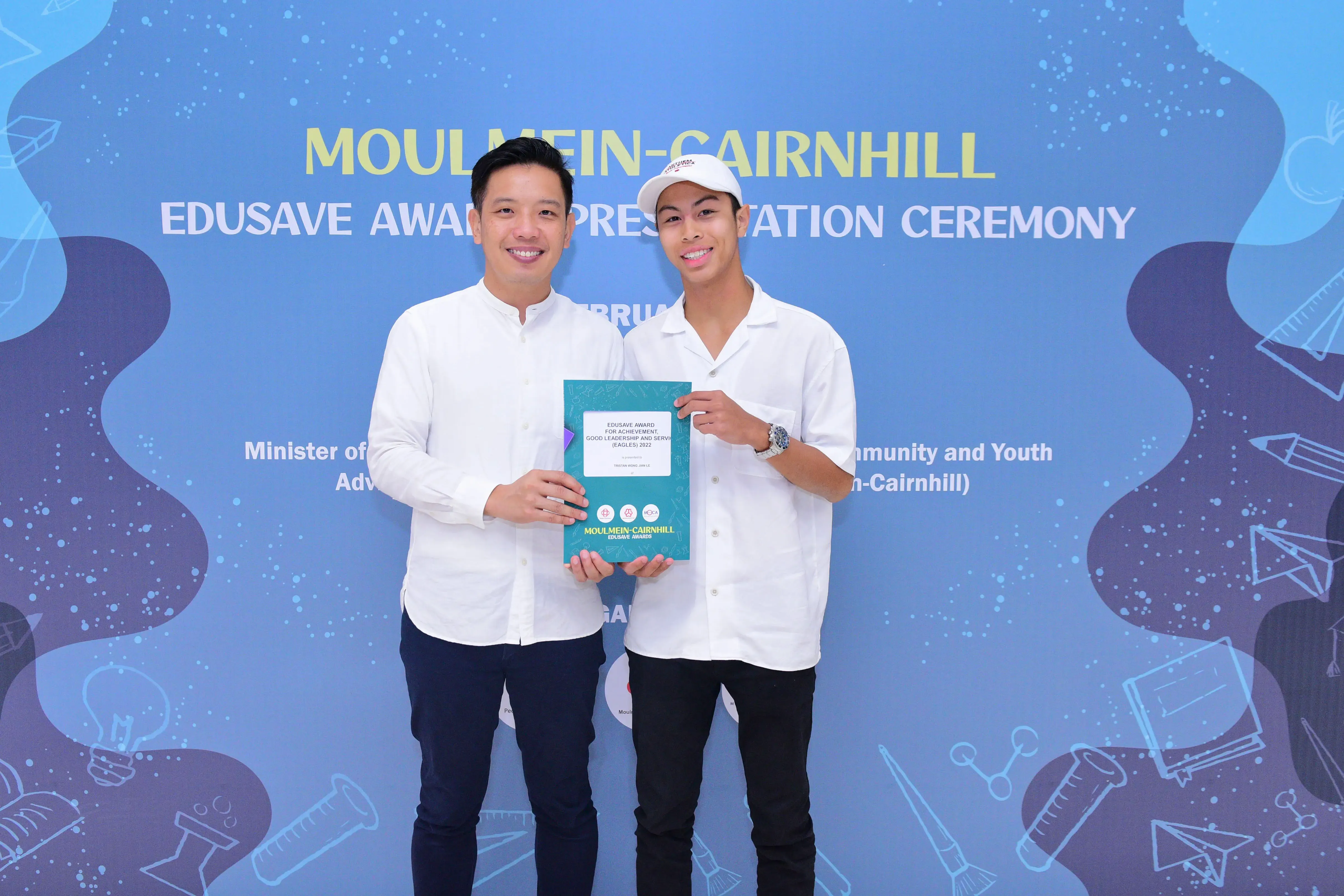 Two men in white shirts hold a teal certificate at the Moulmein-Cairnhill Edusave Award Presentation Ceremony.