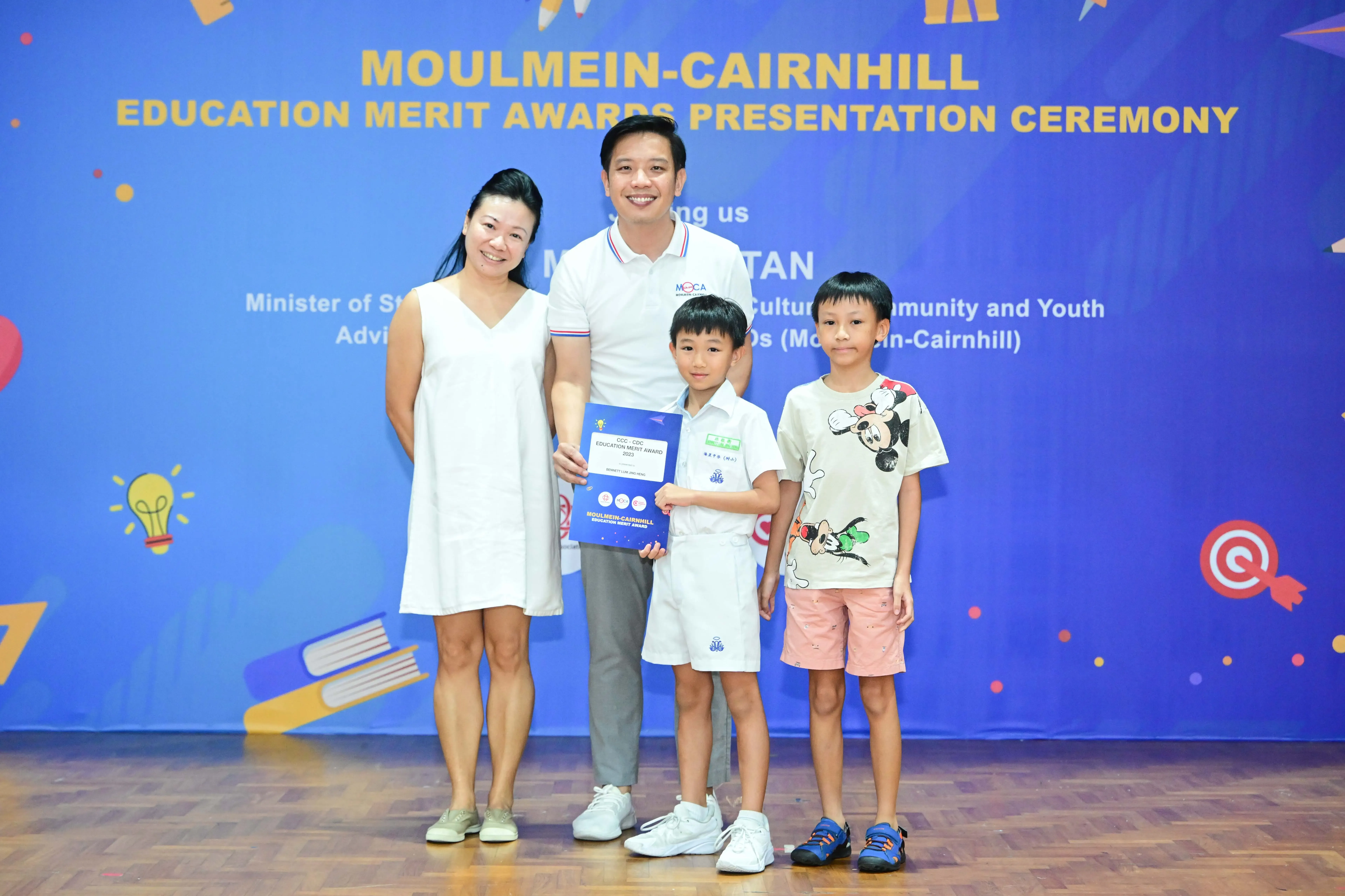 Two adults and two children pose holding an award certificate at the Moulmein-Cairnhill Education Merit Awards Ceremony.