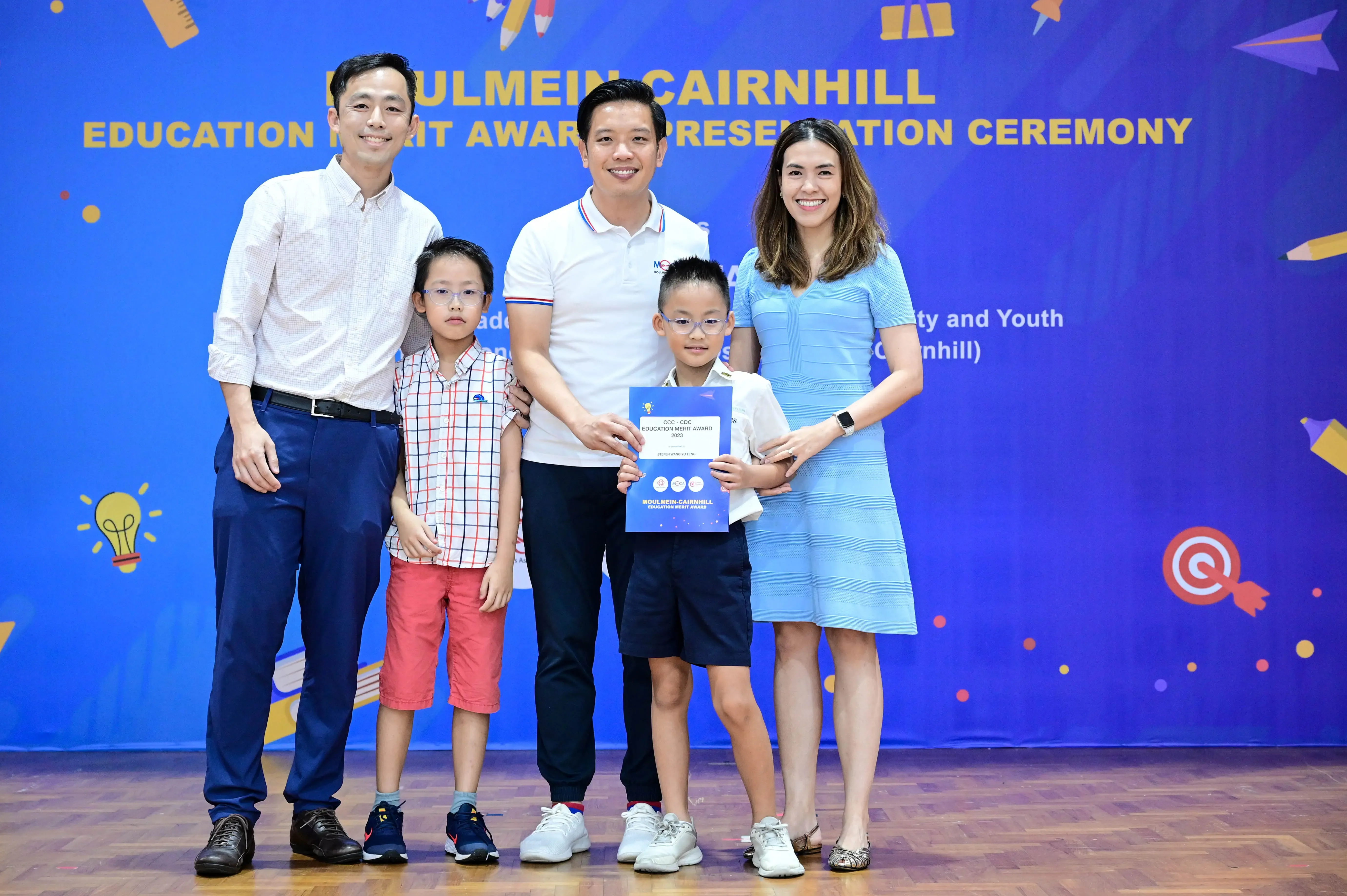 Five people pose at the Moulmein-Cairnhill Education Merit Award Presentation Ceremony, with a boy holding a certificate.