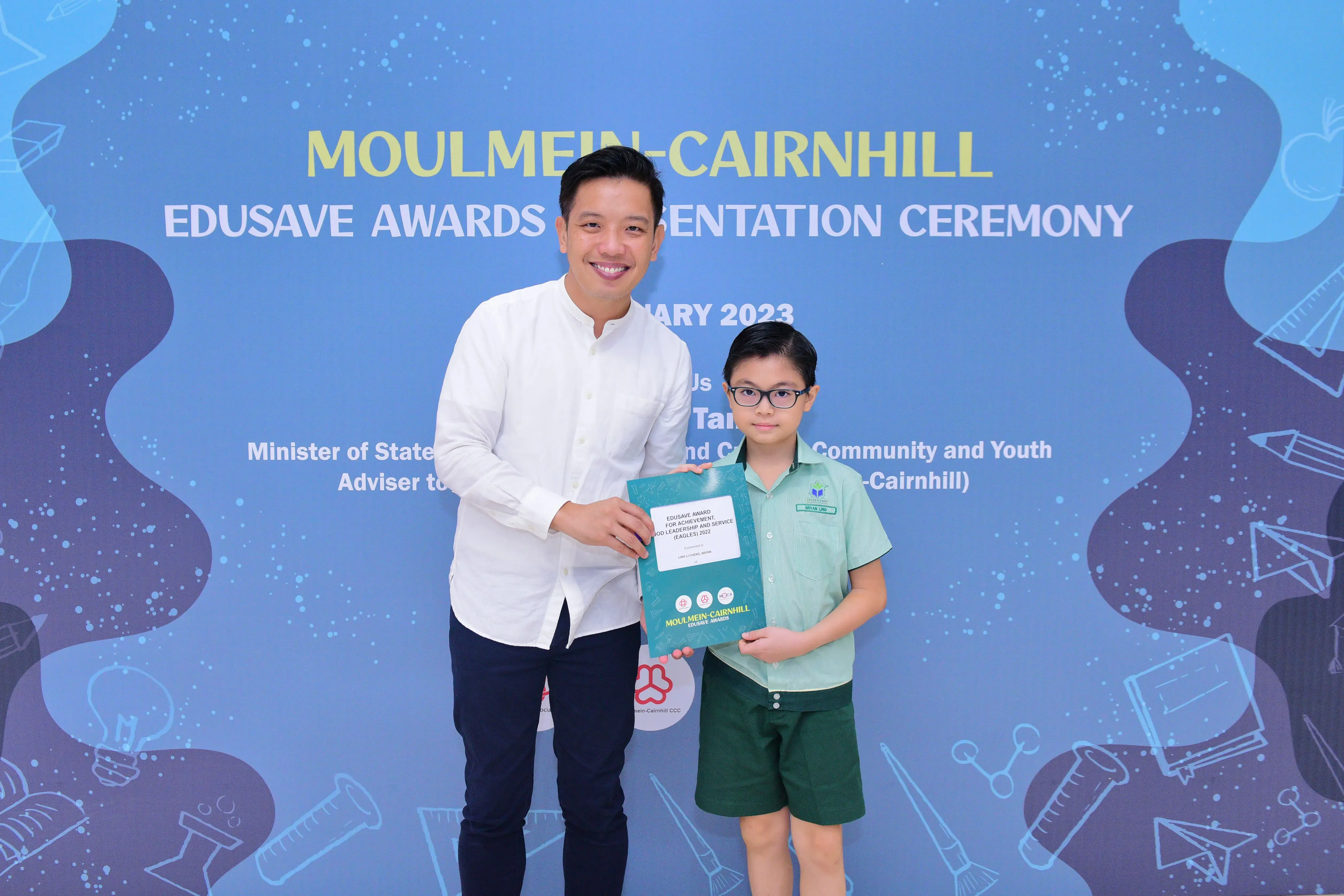 Man and young student holding a certificate at the Moulmein-Cairnhill Edusave Awards Presentation Ceremony 2023.
