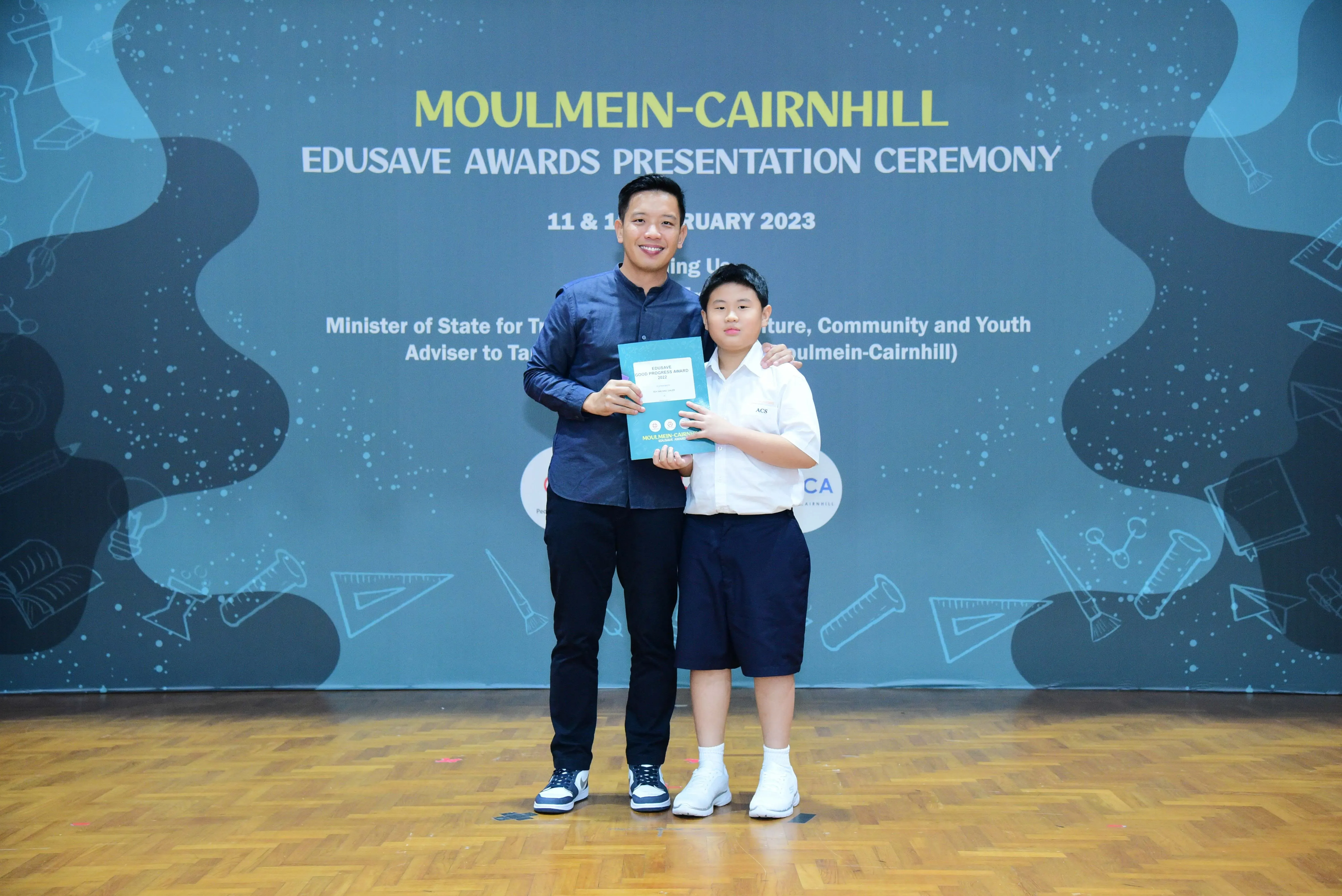 An adult and a young student pose together holding an award at the Moulmein-Cairnhill Edusave Awards Ceremony 2023.