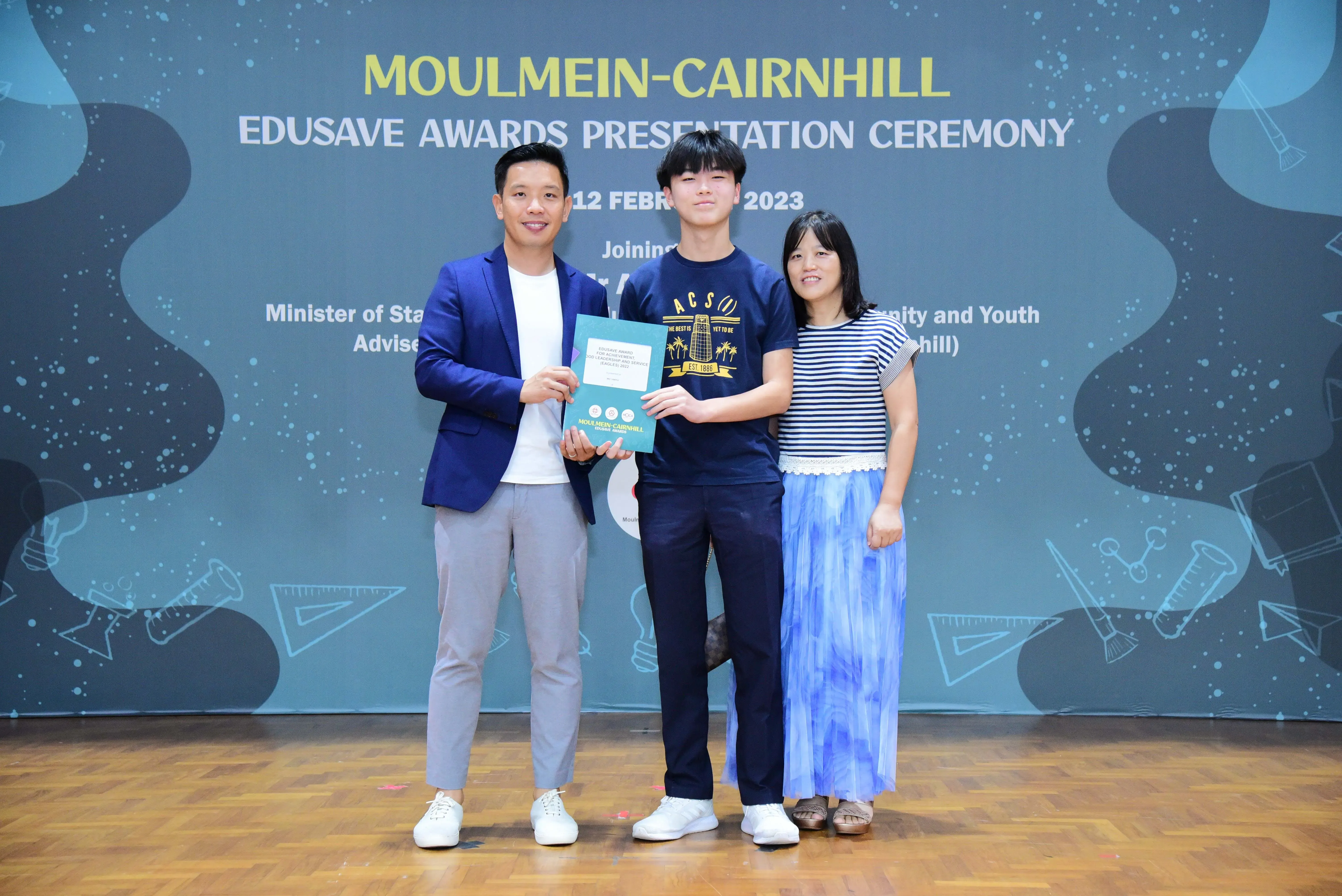 Three people pose on a stage at the Moulmein-Cairnhill Edusave Awards Presentation Ceremony on 12 February 2023.