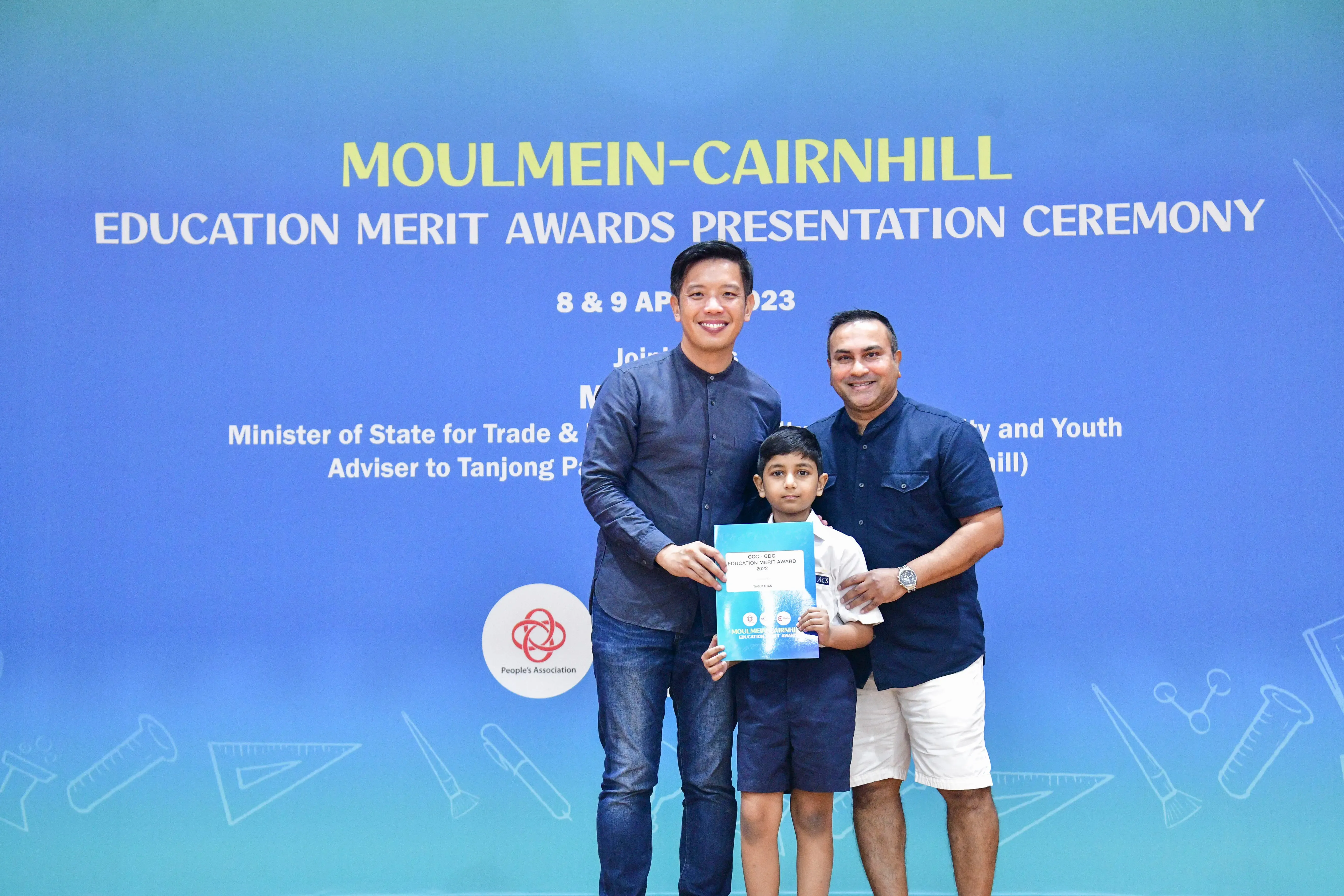 Two men and a young boy hold a certificate at the Moulmein-Cairnhill Education Merit Awards Ceremony, April 2023.