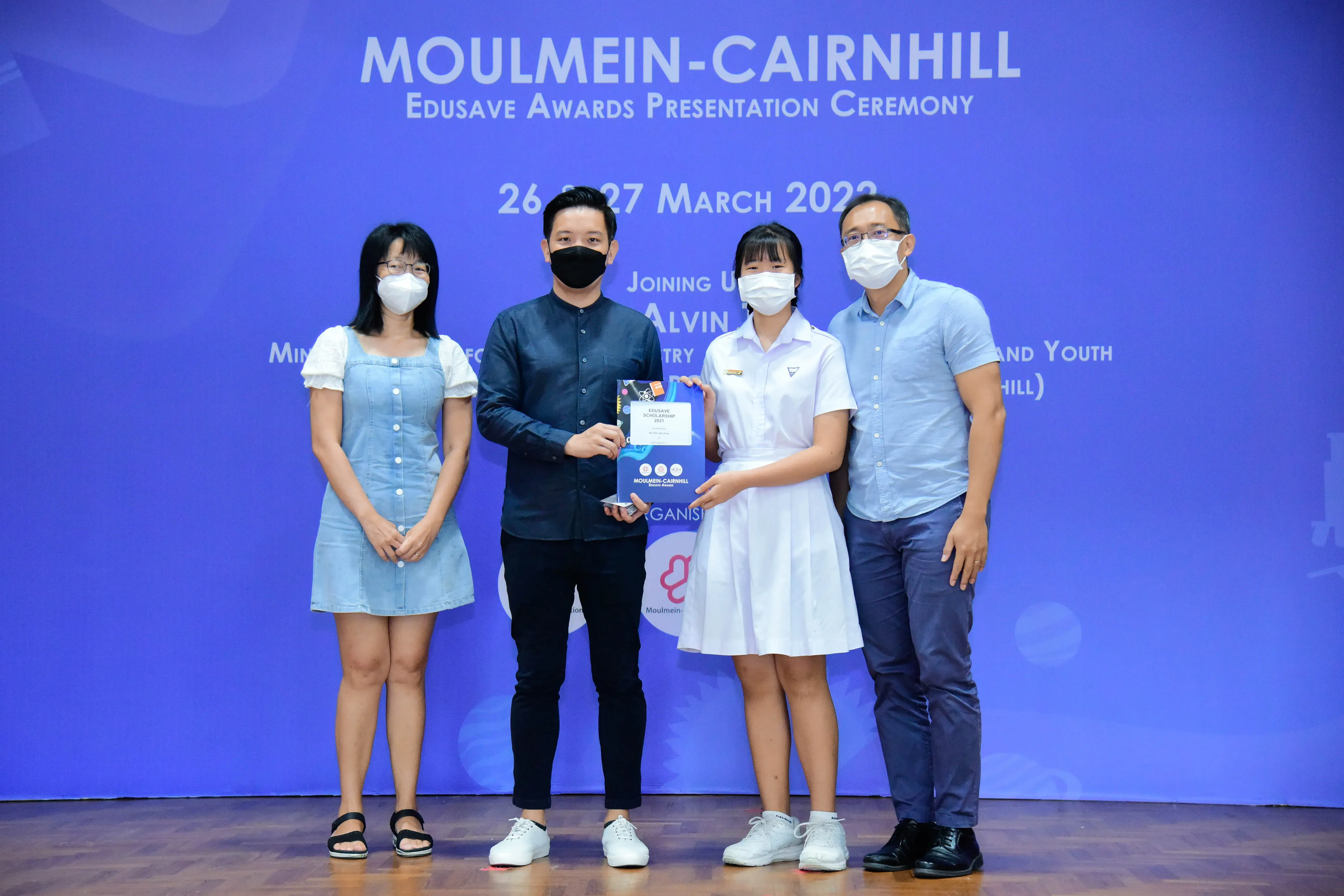 Four masked people stand on a stage at the Moulmein-Cairnhill Edusave Awards Presentation Ceremony, March 2022.