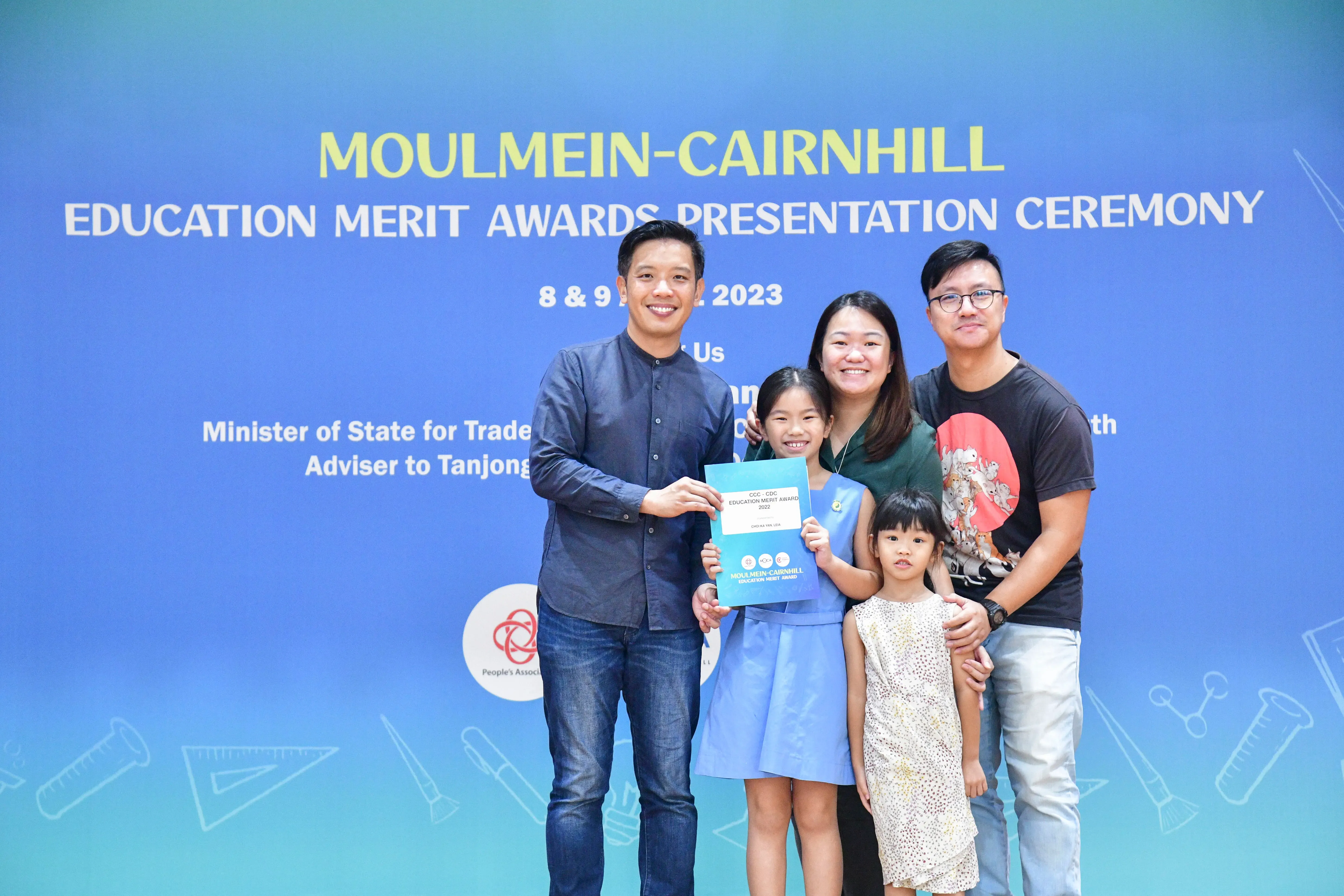 A family of four poses with a man holding a certificate at the Moulmein-Cairnhill Education Merit Awards 2023.