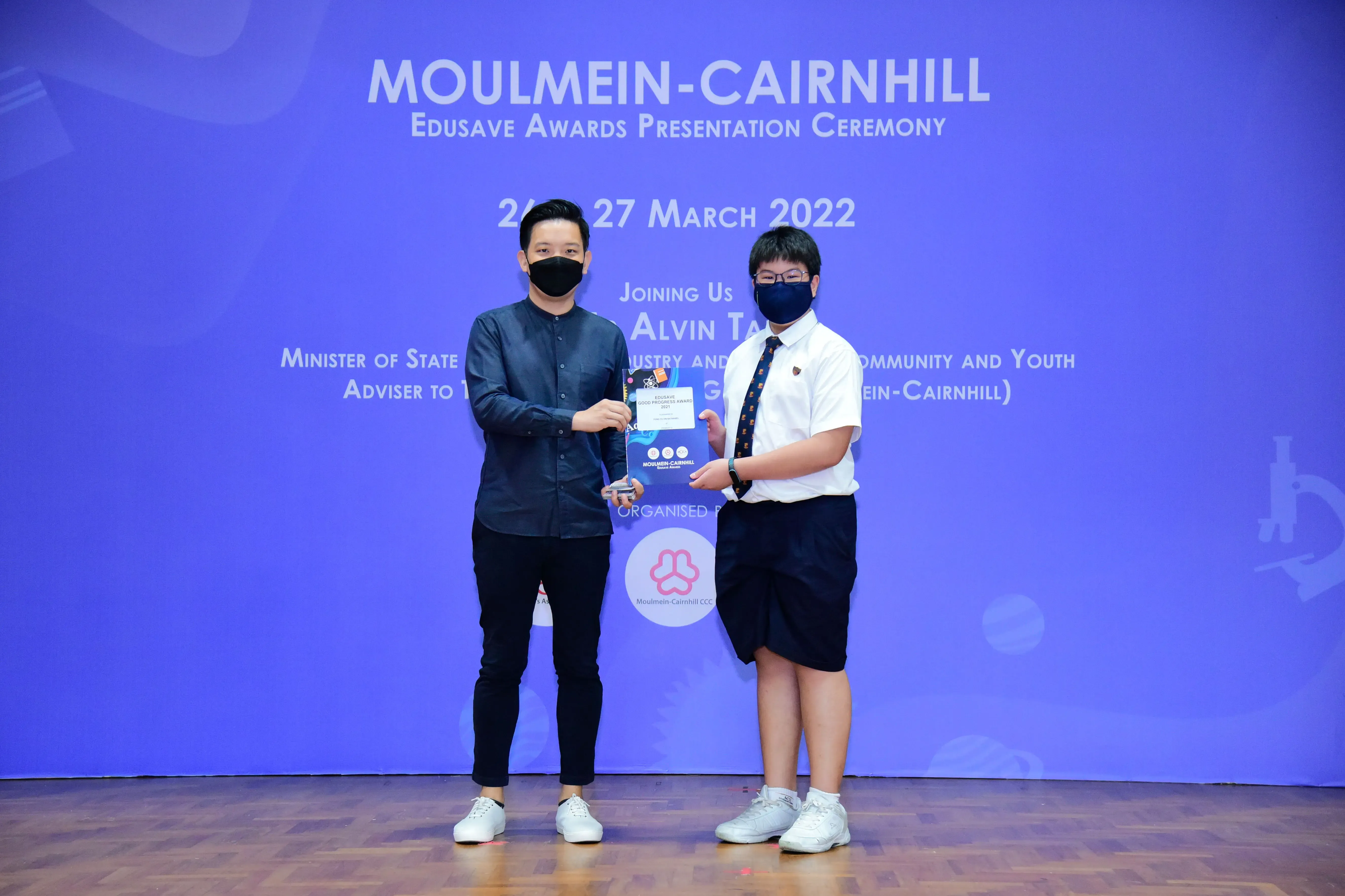 Two masked individuals hold an award at the Moulmein-Cairnhill Edusave Awards Presentation Ceremony, March 2022.