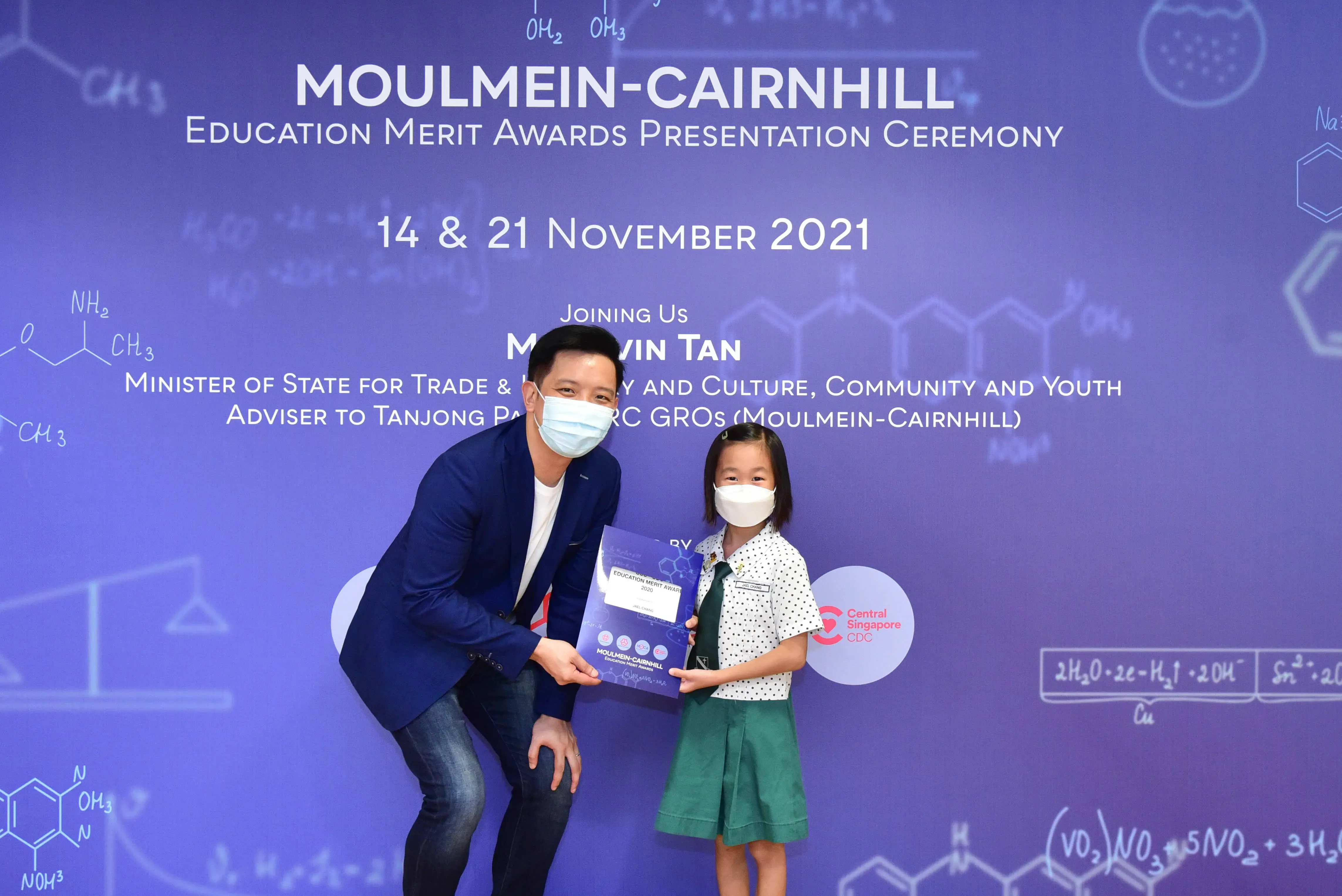 A masked man and young girl hold an award at the Moulmein-Cairnhill Education Merit Awards Ceremony, November 2021.