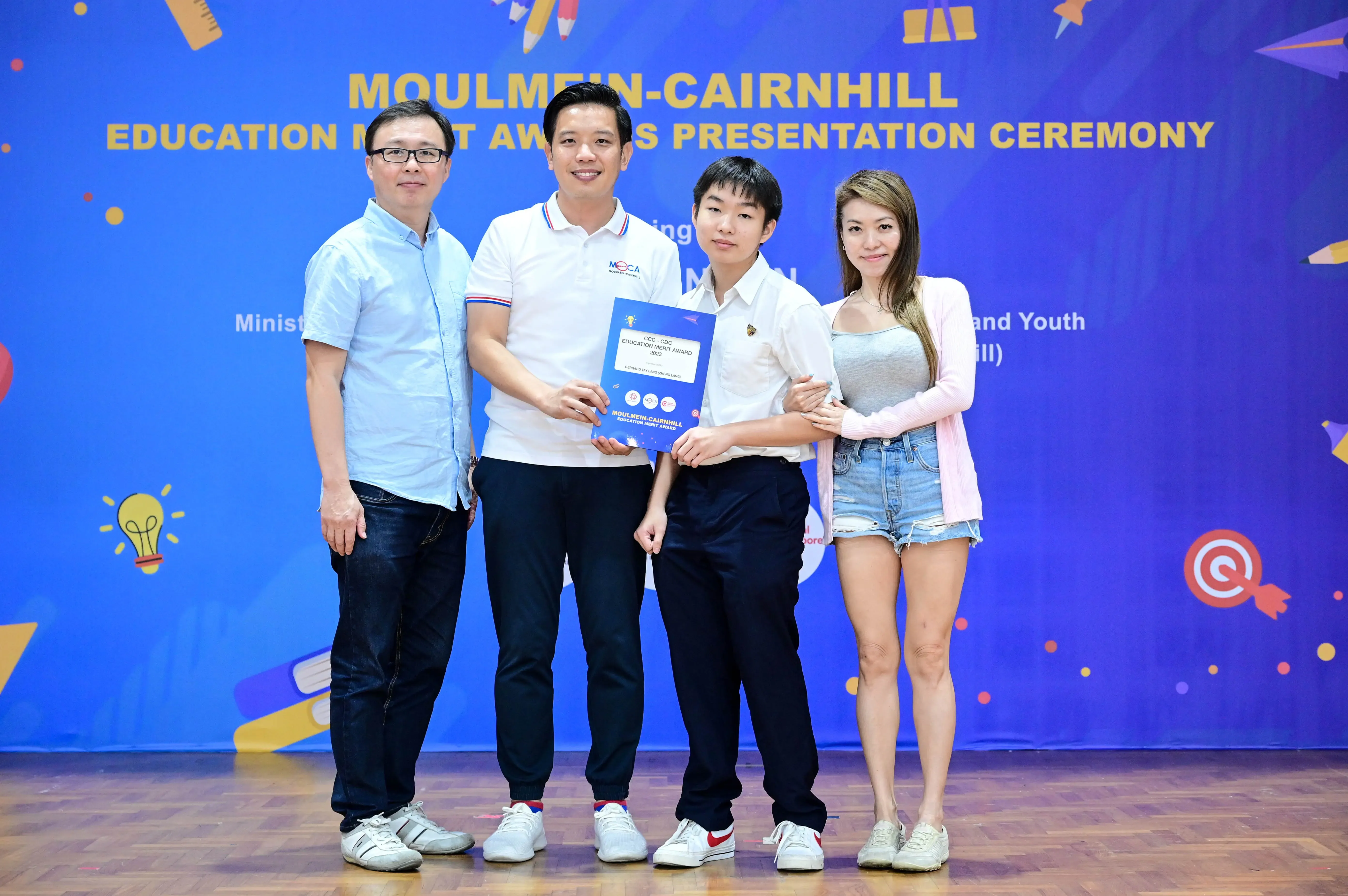 Four people pose together holding an award certificate at the Moulmein-Cairnhill Education Merit Awards Presentation Ceremony.