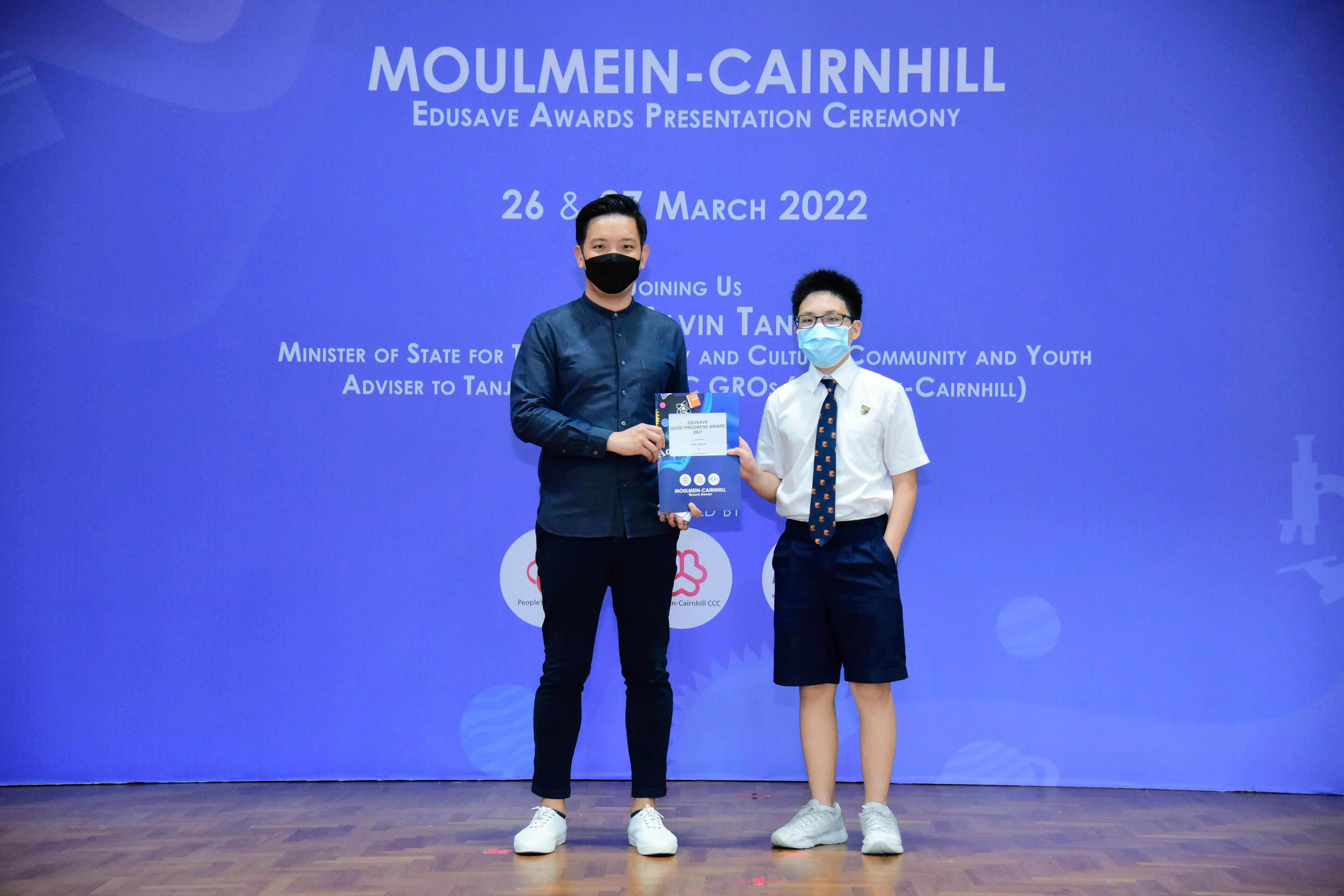 Two masked individuals hold an award at the Moulmein-Cairnhill Edusave Awards Presentation Ceremony, March 2022.