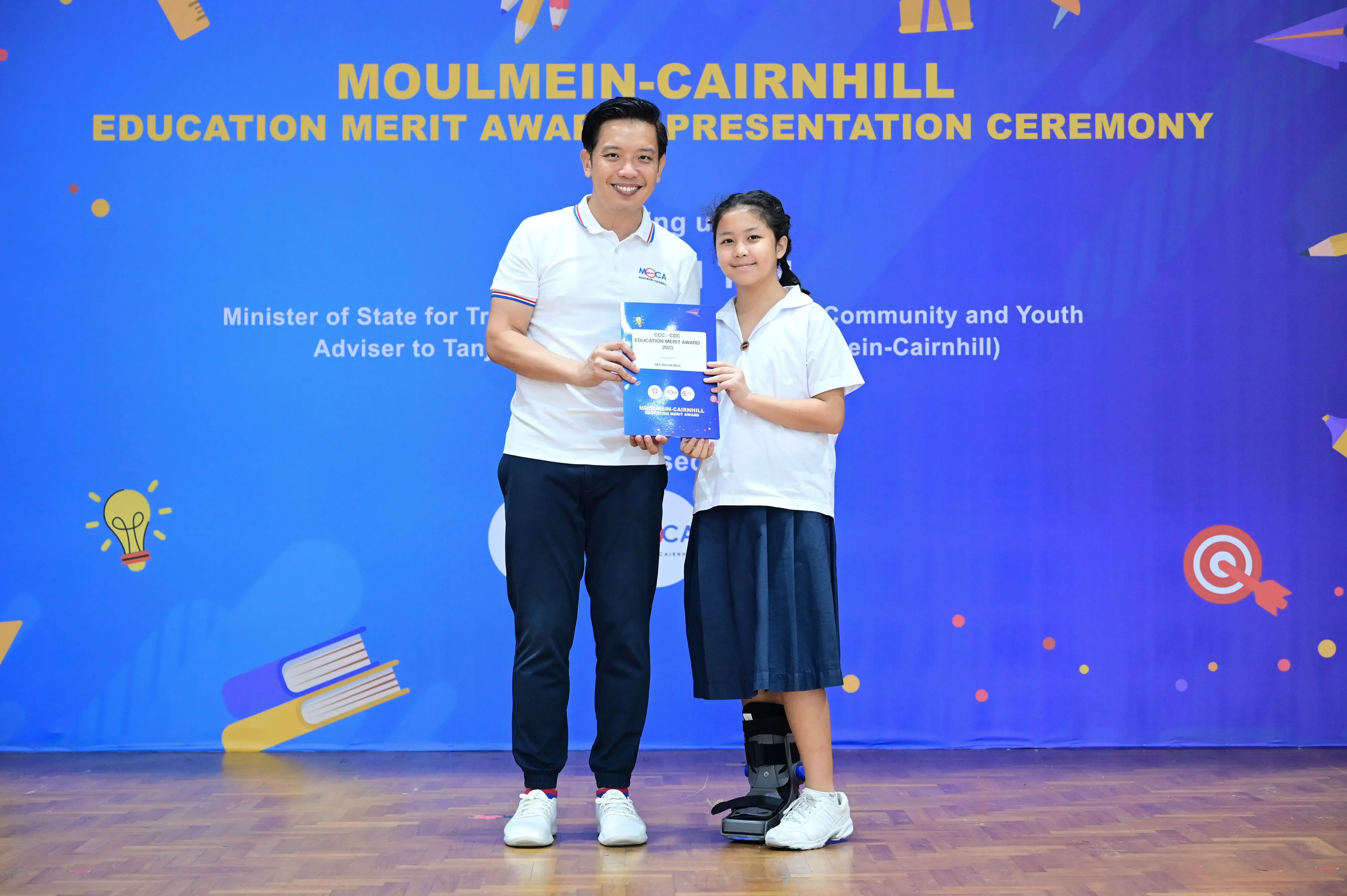 A man and a young girl hold an award certificate at the Moulmein-Cairnhill Education Merit Award Presentation Ceremony.