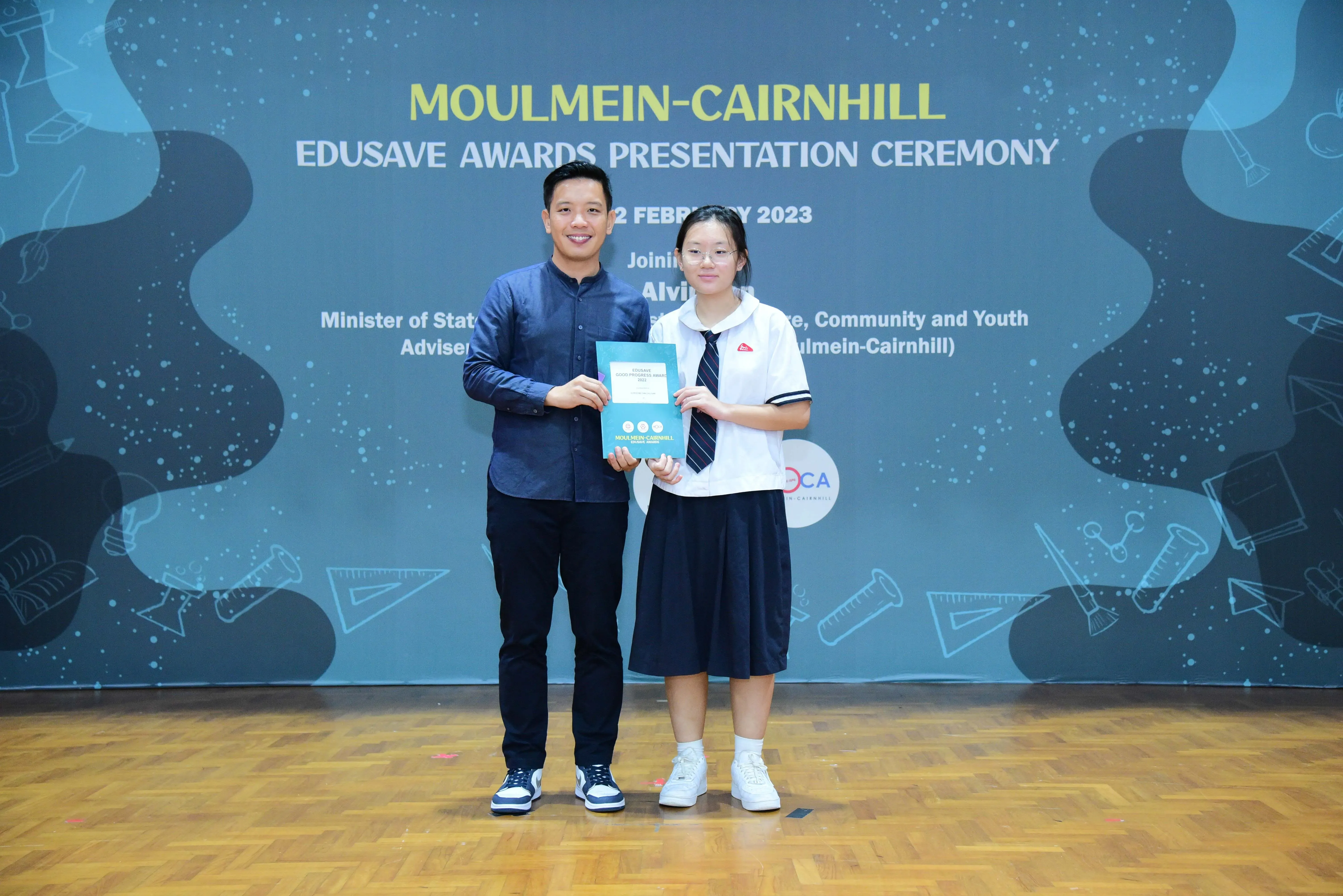A man and a female student in uniform hold a certificate at the Moulmein-Cairnhill Edusave Awards Ceremony 2023.