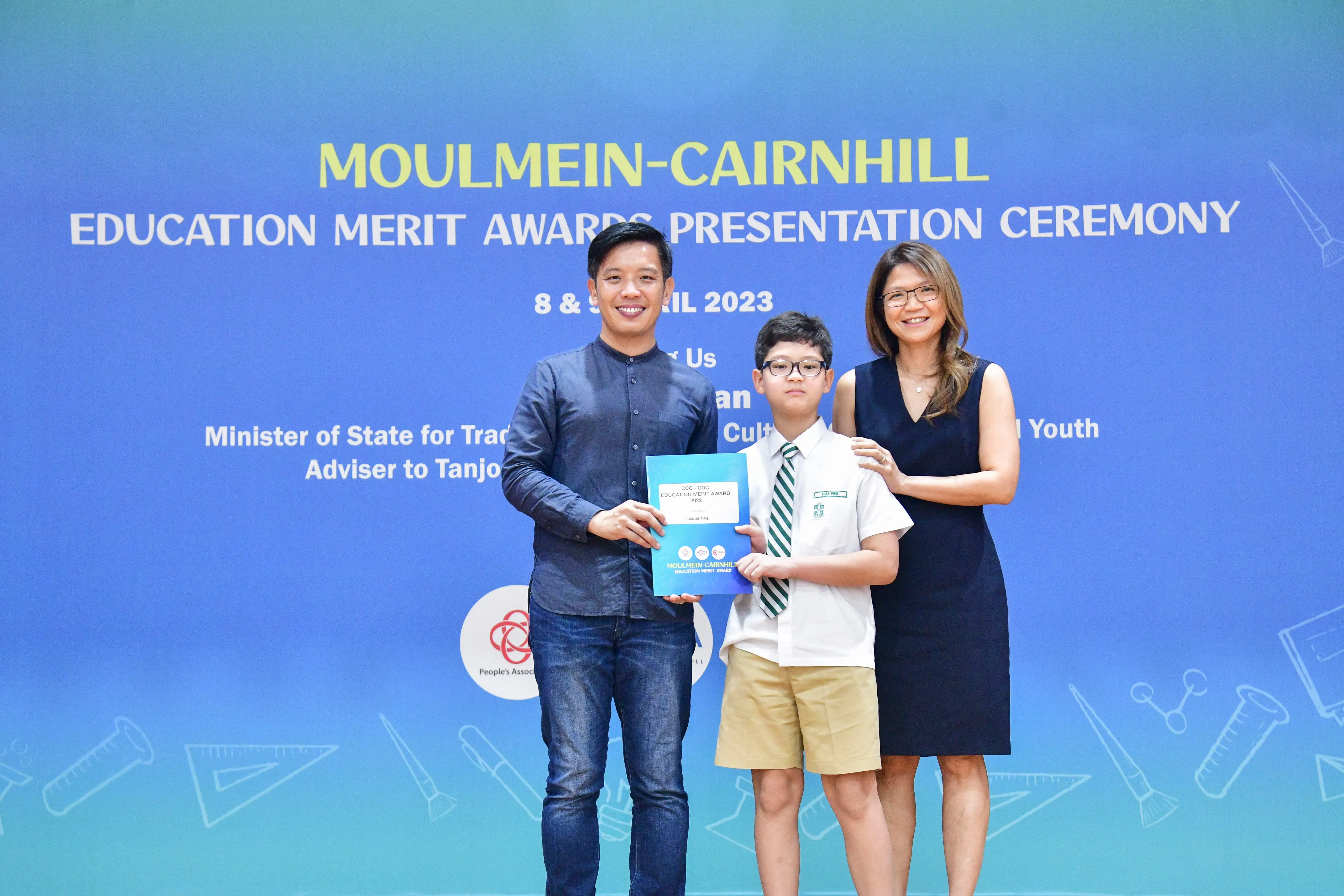 A man, a young boy holding a certificate, and a woman pose at the Moulmein-Cairnhill Education Merit Awards 2023.