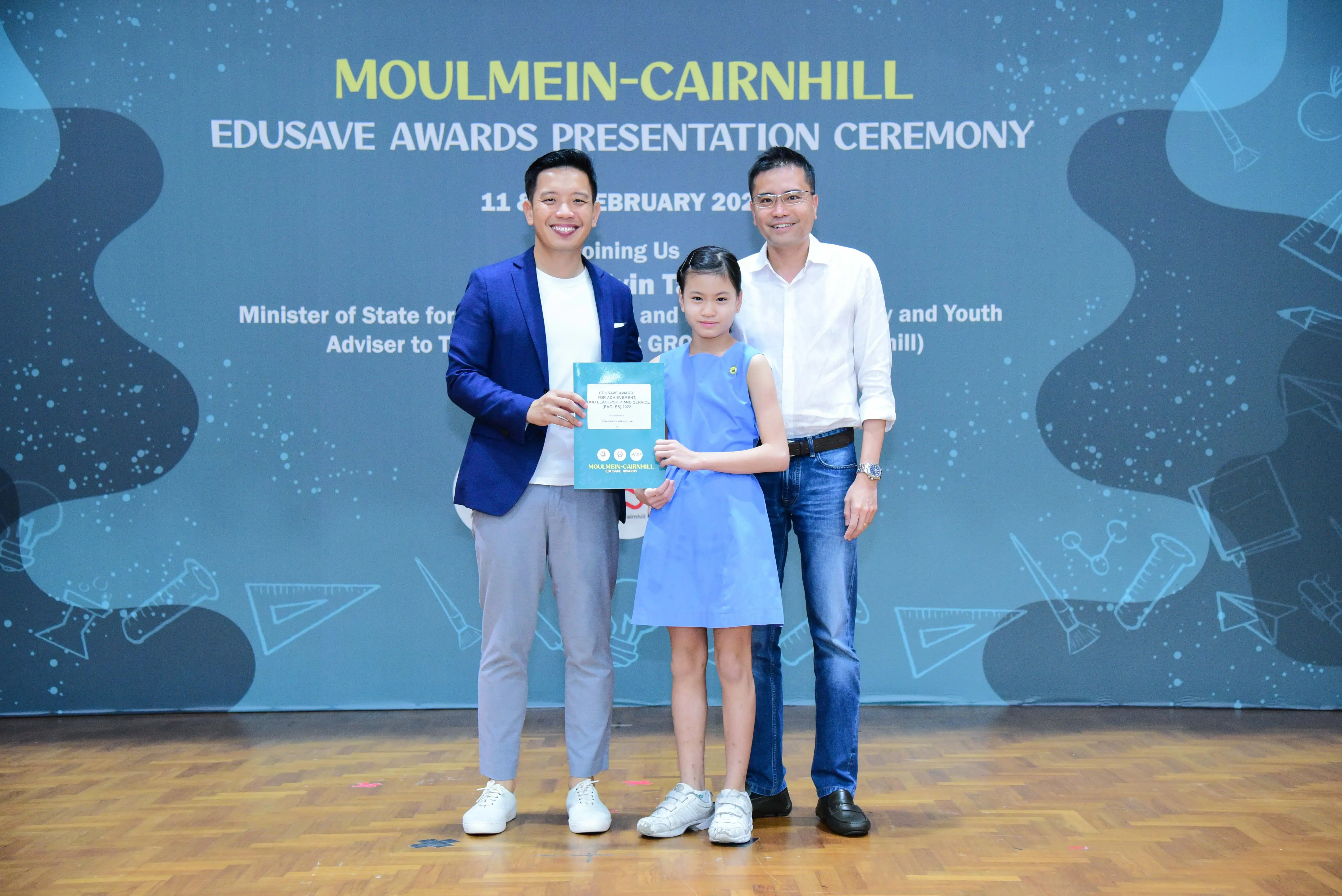 Two men and a girl in a blue dress pose at the Moulmein-Cairnhill Edusave Awards Presentation Ceremony.