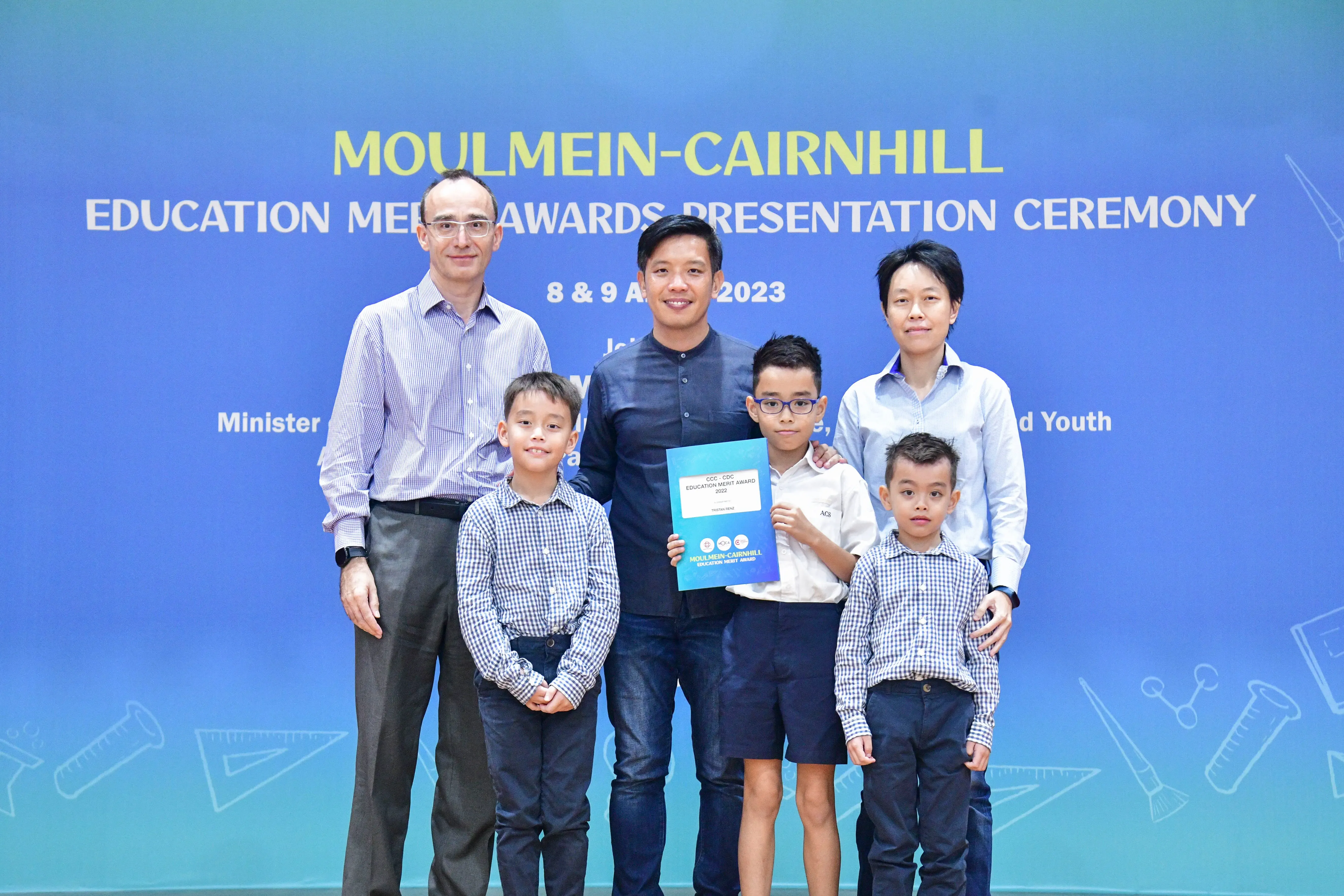 Five people pose at the Moulmein-Cairnhill Education Merit Awards Presentation Ceremony 2023, with a boy holding a certificate.